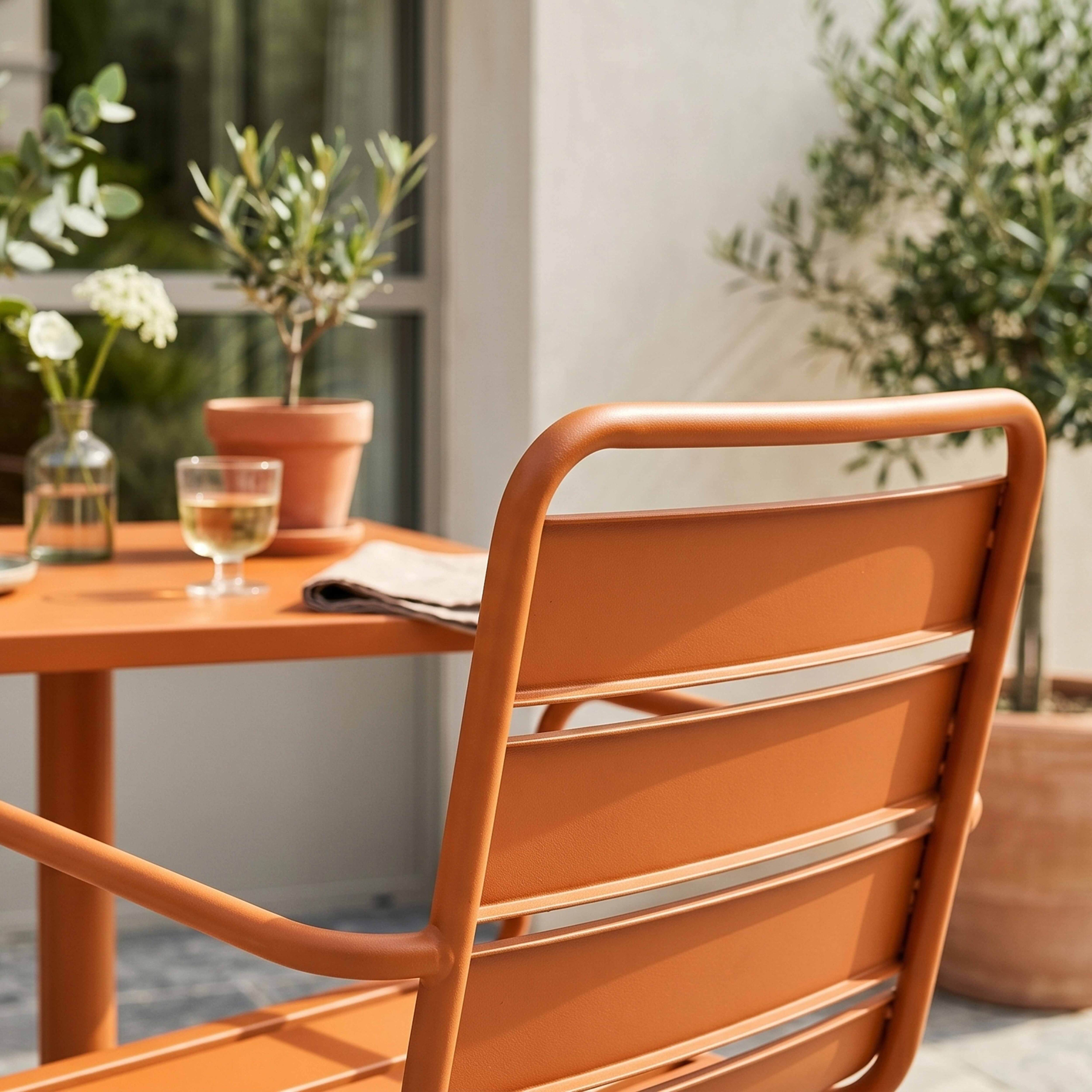 Orange Stuhllehne mit Tisch, Glas und Pflanzen im Freien.
