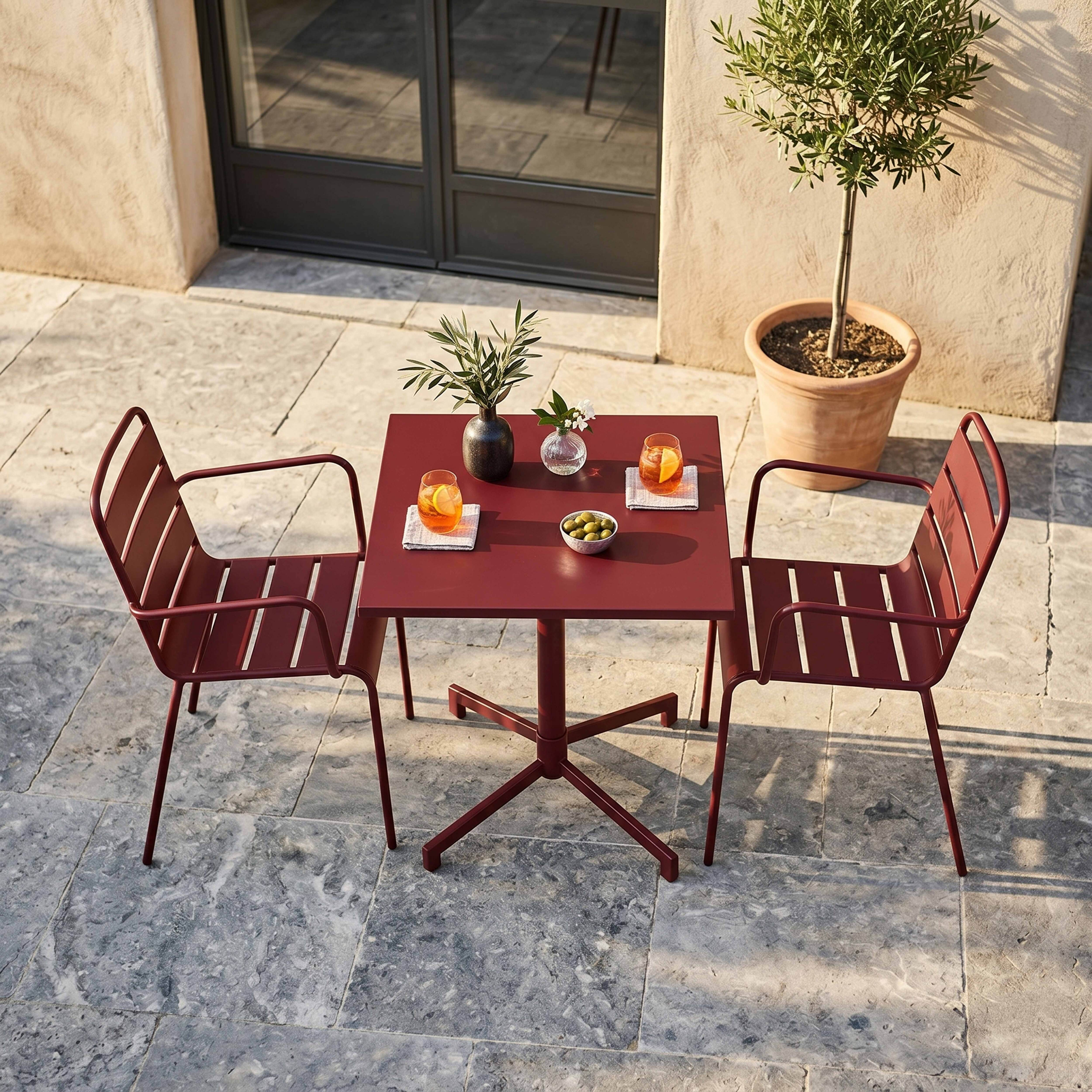Ein rotes Gartentischset mit zwei Stühlen, zwei Gläsern und Oliven.