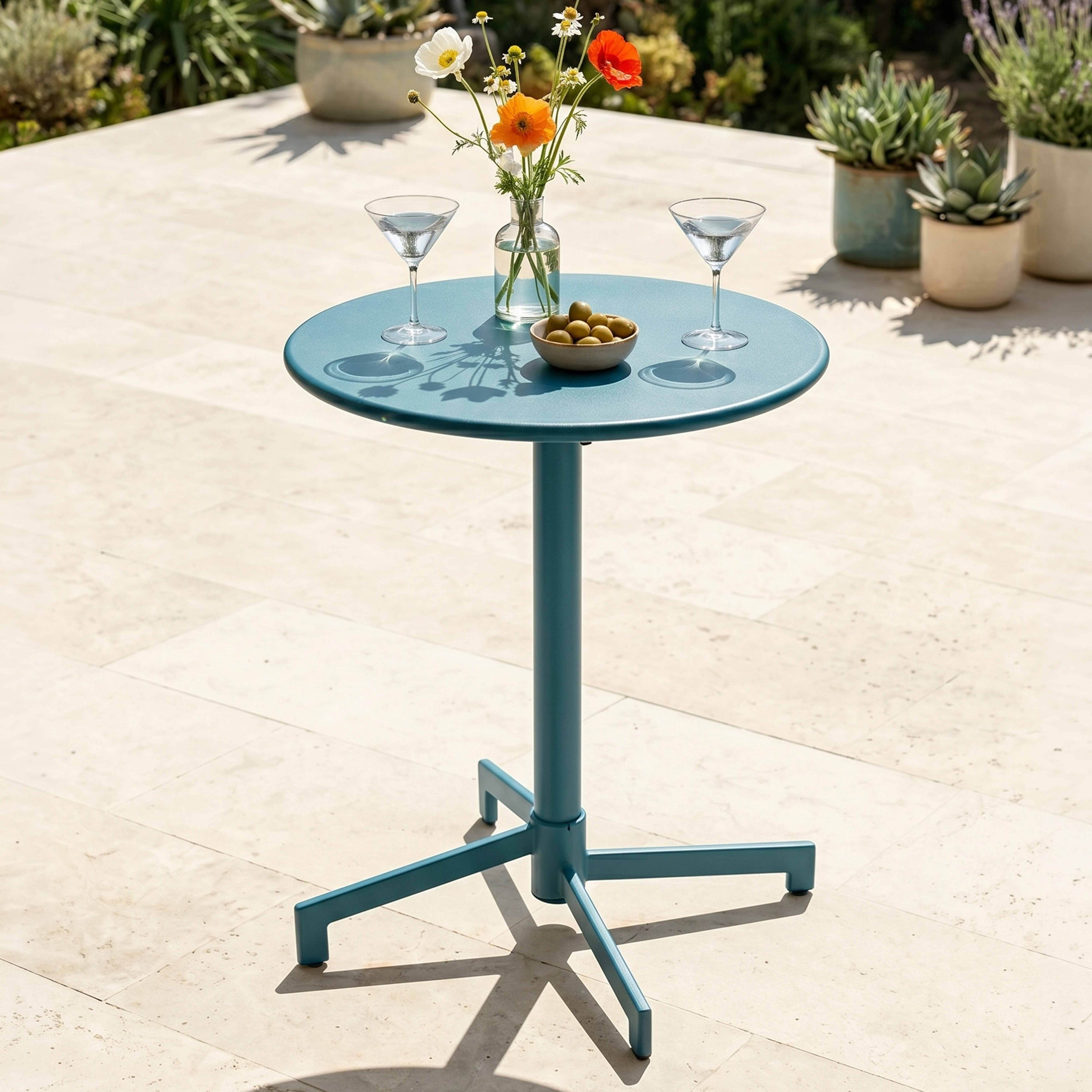 Ein blauer Tisch im Freien mit Blumen, Oliven und Martinigläsern.