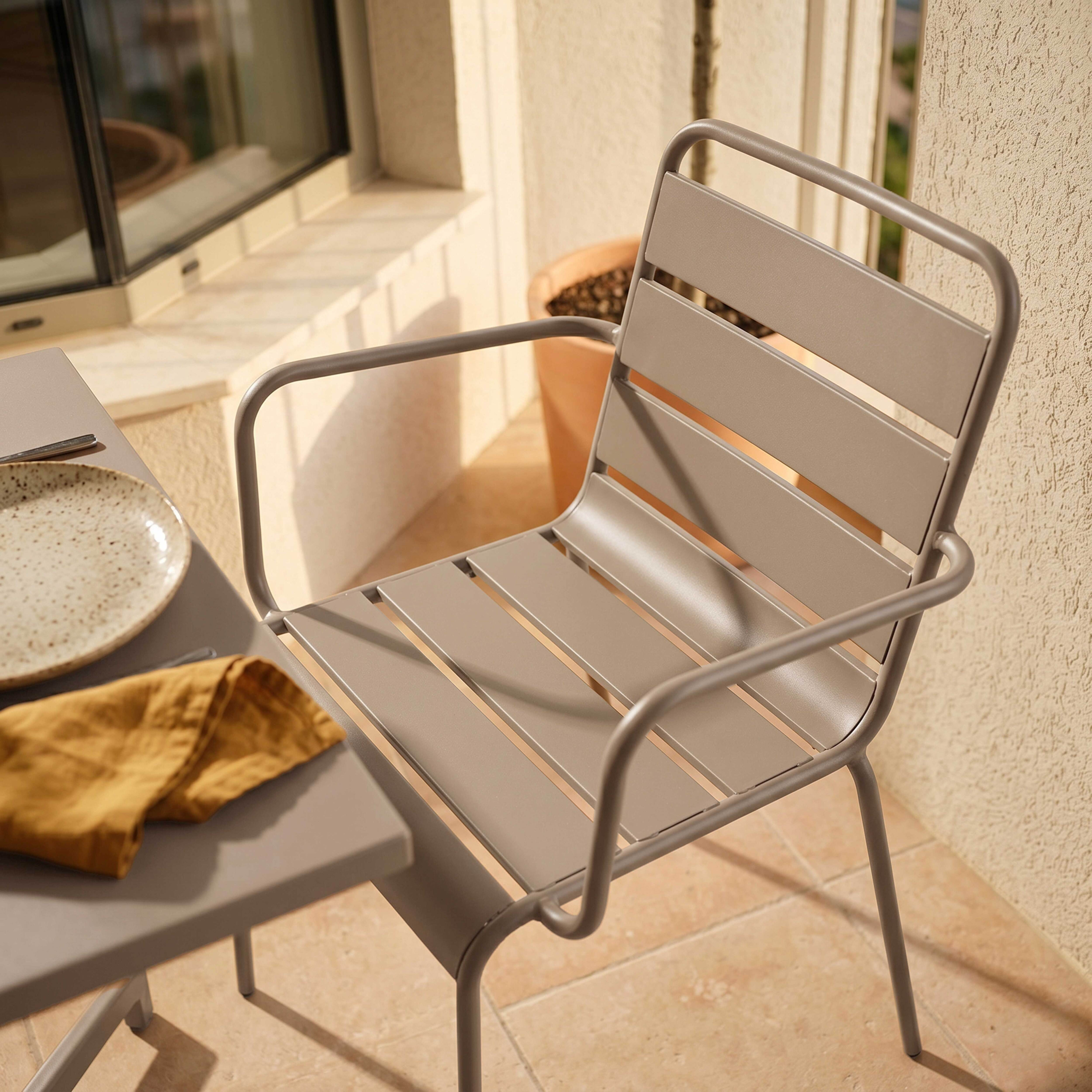 Grauer Stuhl und Tisch mit gelber Serviette und Teller auf einer Terrasse.