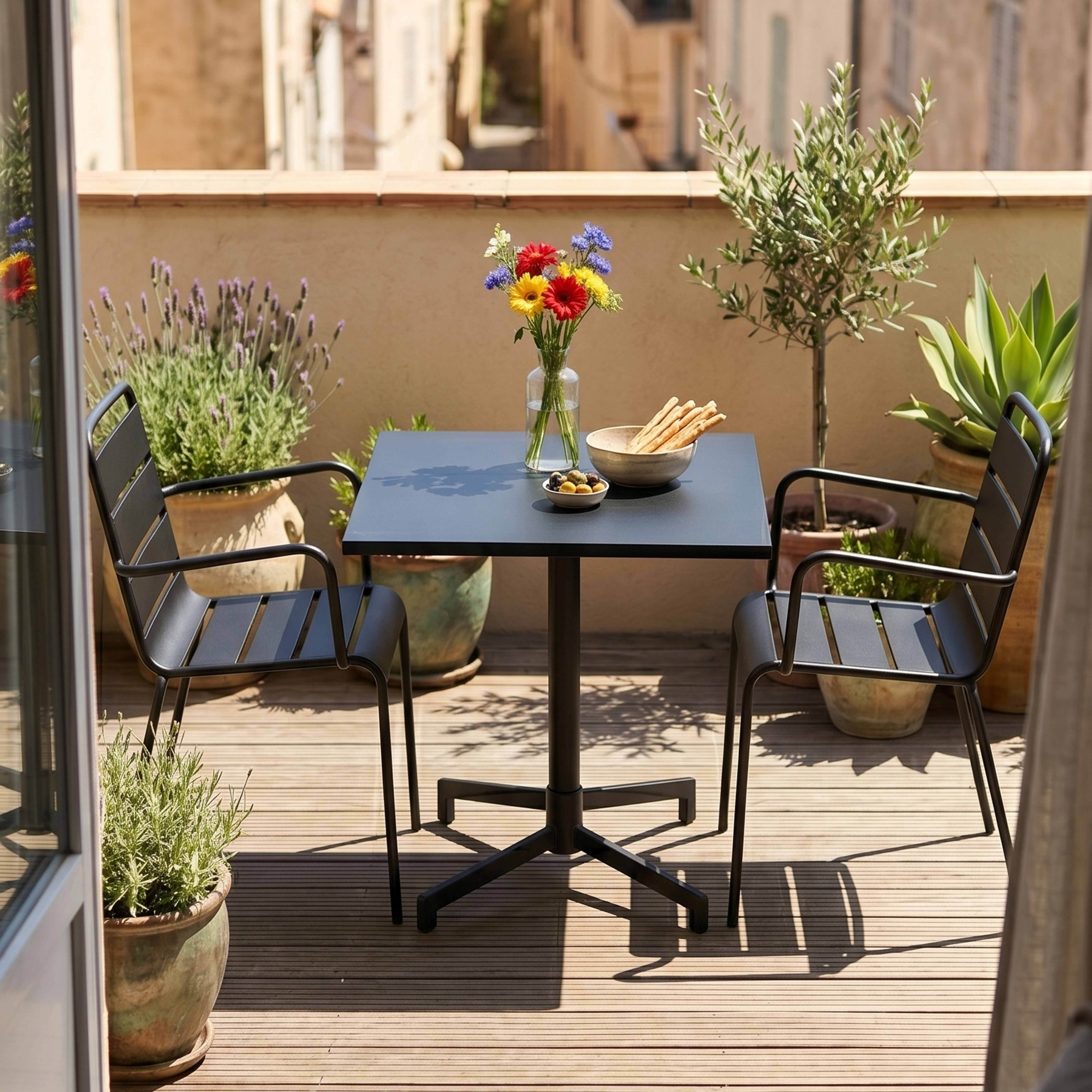 Ein runder Tisch mit zwei Stühlen auf einem Balkon mit Pflanzen und Blumen.