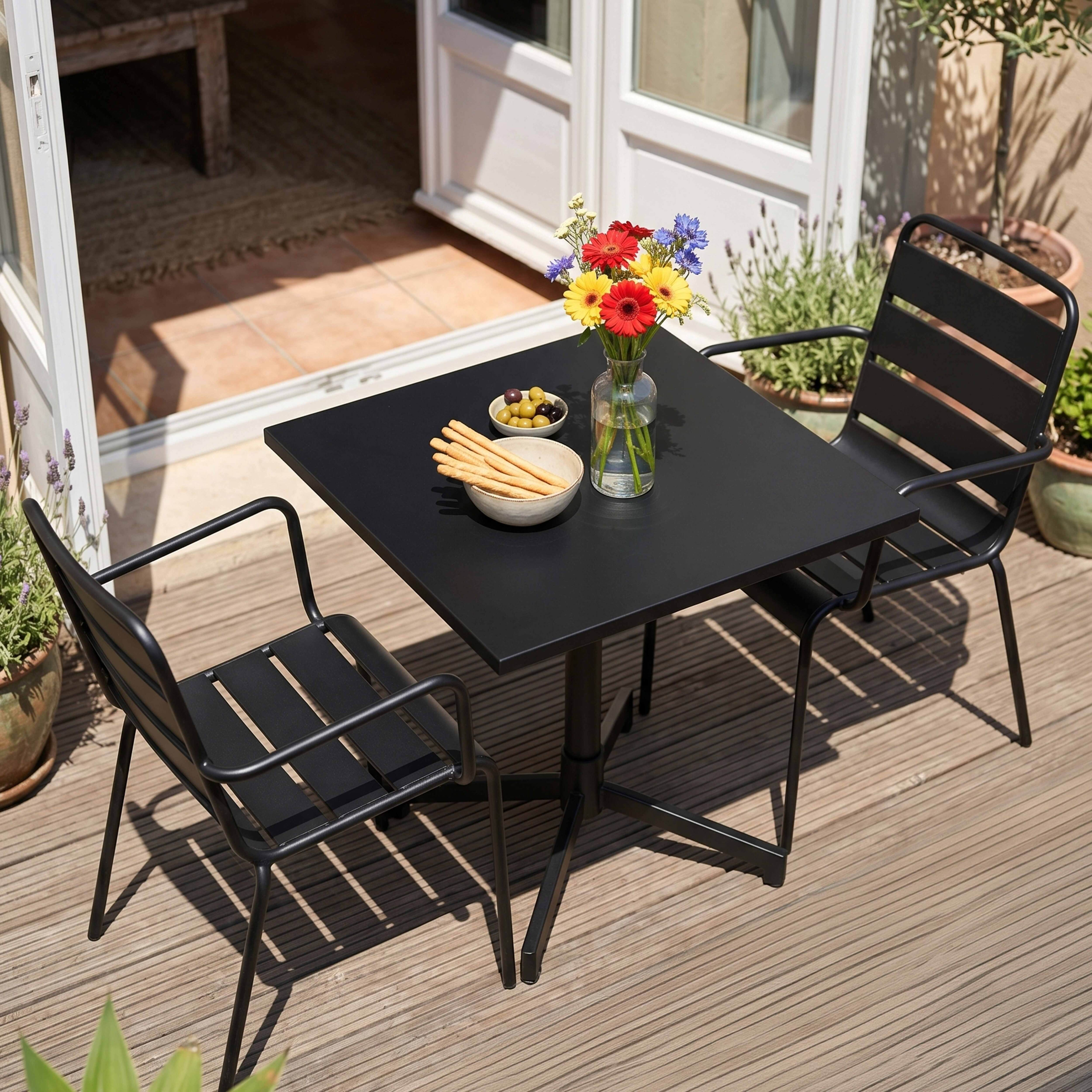 Ein schwarzer Gartentisch mit Blumen, Oliven und Grissini steht auf einer Holzterrasse.