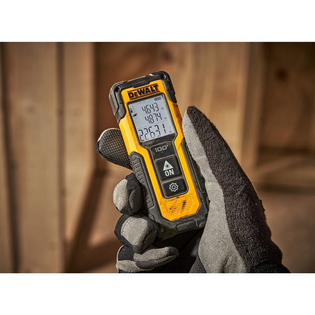 Eine Hand in einem grauen Handschuh hält ein gelbes DeWalt-Messgerät mit einem digitalen Display.