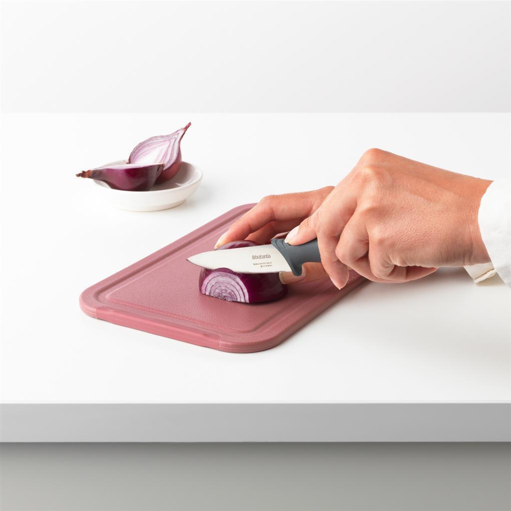 Une main coupe un oignon rouge sur une planche à découper avec un couteau.