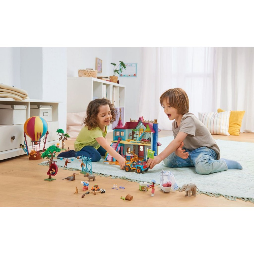 Dos niños juegan con una casa de juguete y varias figuras, incluidos animales y un globo aerostático.