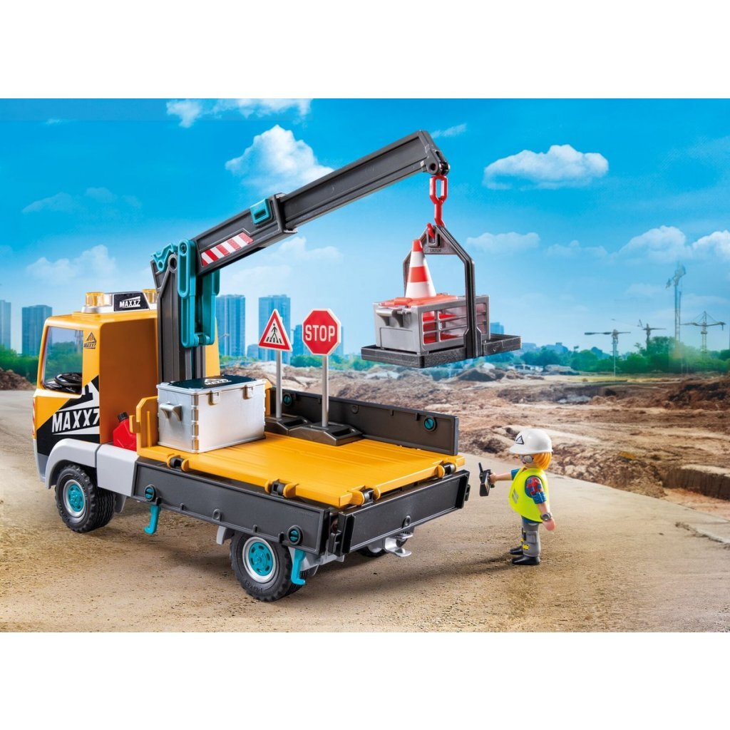 Un camion da cantiere con gru solleva un cono arancione. Un operaio è vicino.