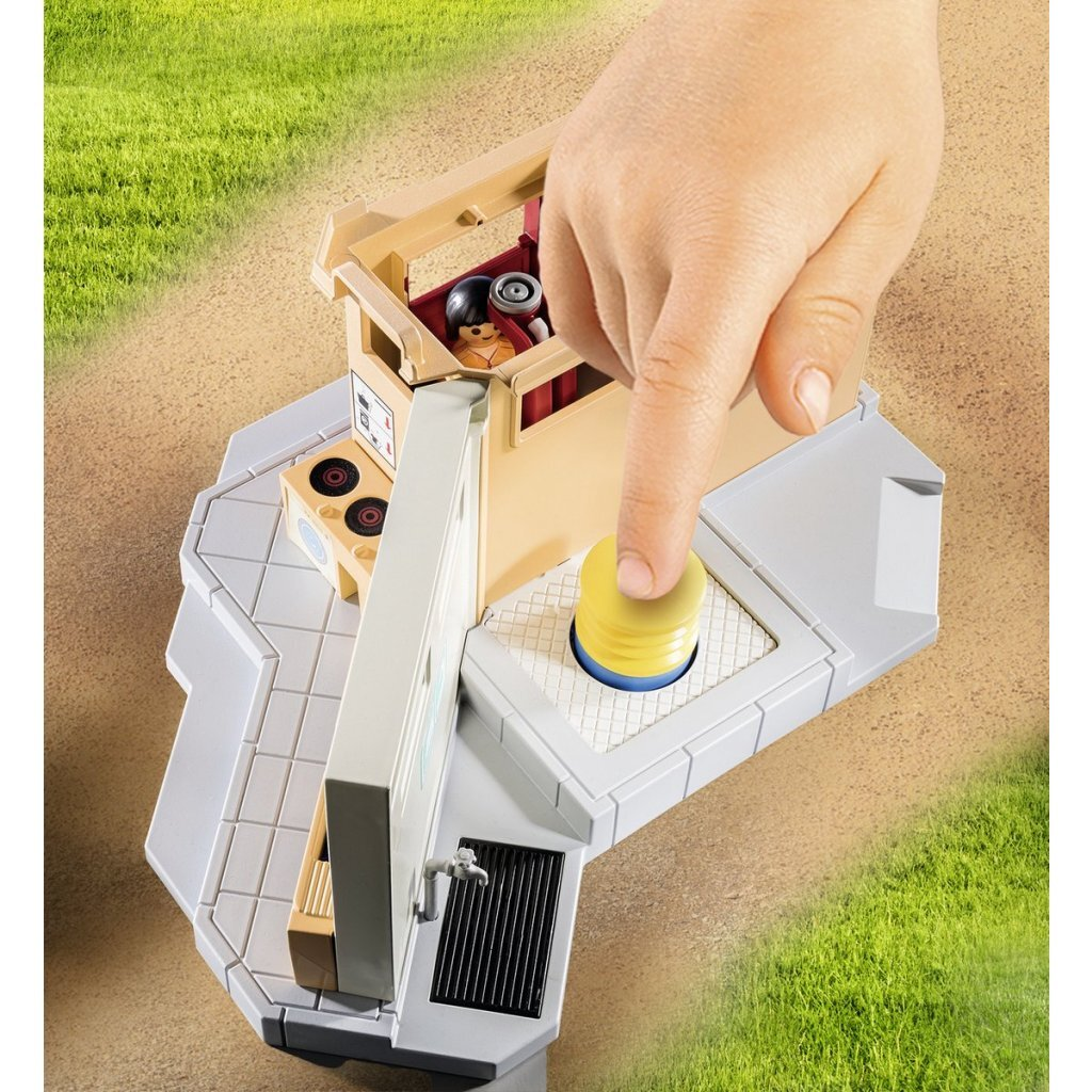 Una mano preme un pulsante giallo su un playset giocattolo con figure e accessori.