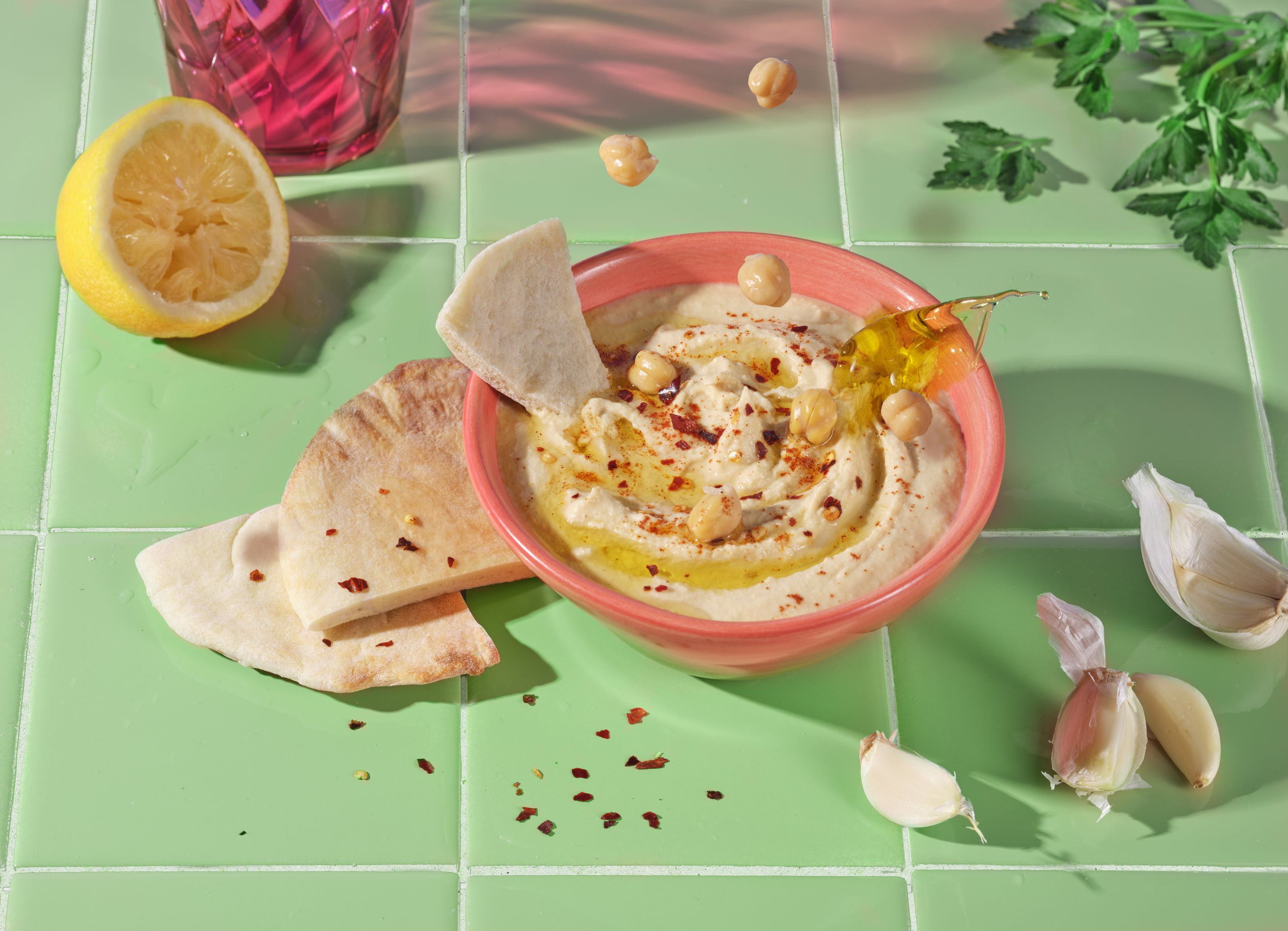 Hummus con pita, limone, aglio e prezzemolo su piastrelle verdi.