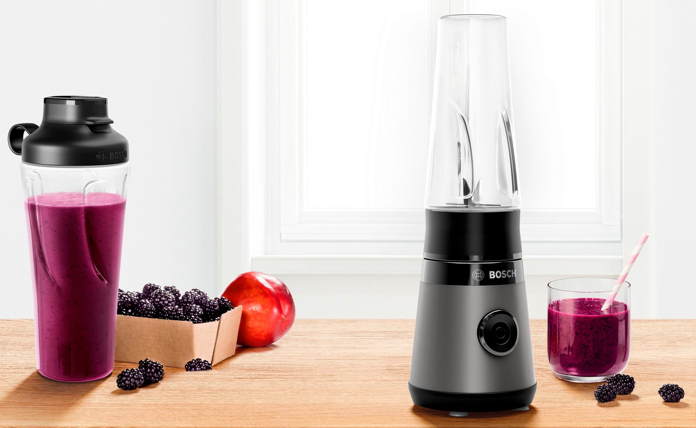 Ein Mixer mit Beeren, einem Apfel und einem Smoothie auf einem Holztisch.