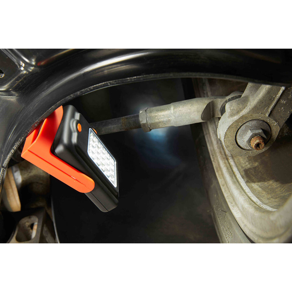 Eine orange-schwarze Arbeitsleuchte beleuchtet eine Autoaufhängung und ein Rad.