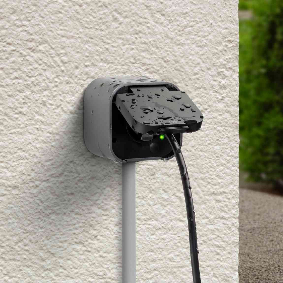 Graue Ladestation mit geöffnetem Deckel, tropfnass, mit grünem Licht und Kabel.