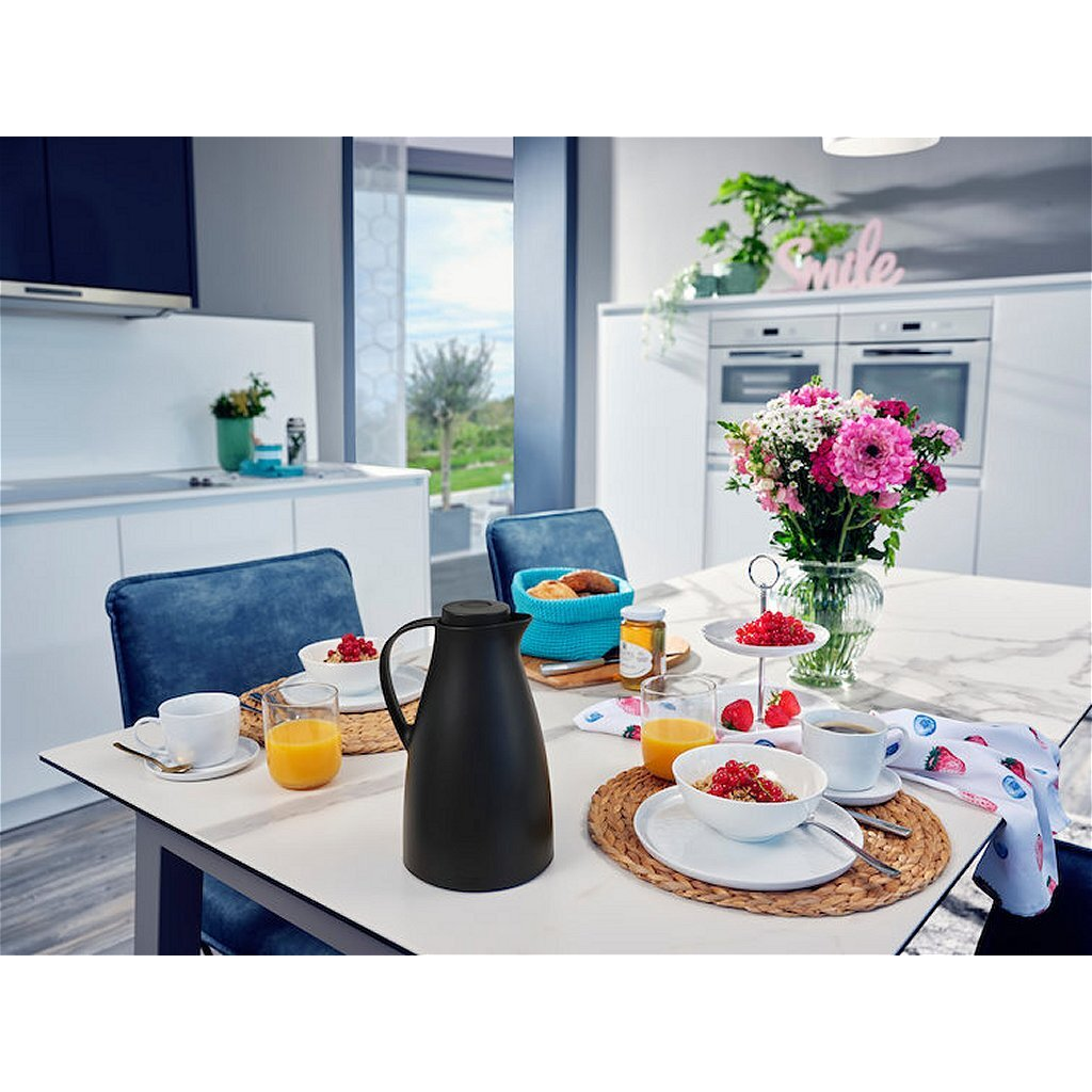 Ein gedeckter Tisch mit Frühstück: Thermoskanne, Saft, Müsli, Kaffee und Blumen.