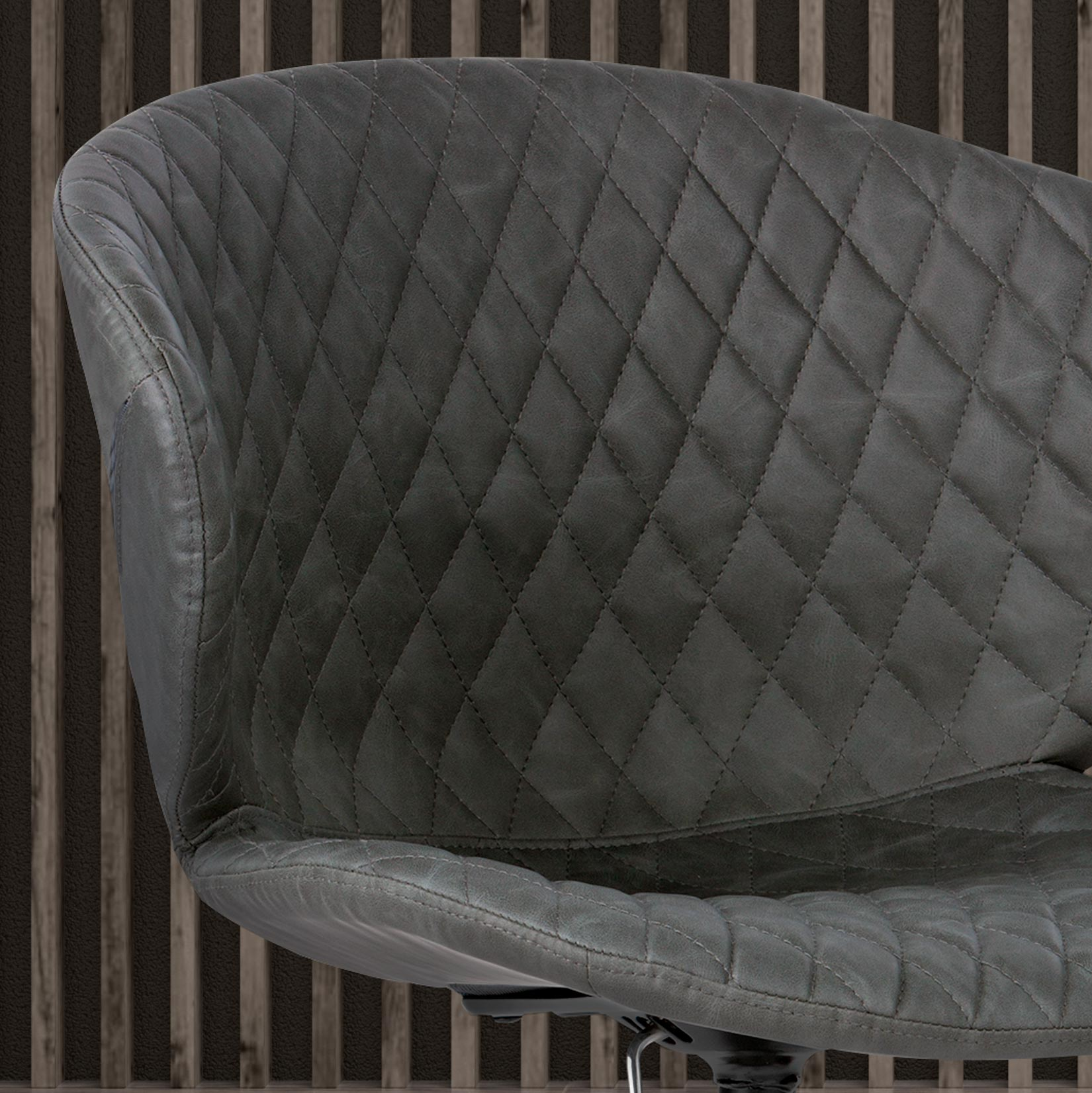 Silla gris acolchada con patrón de diamantes frente a listones de madera verticales.