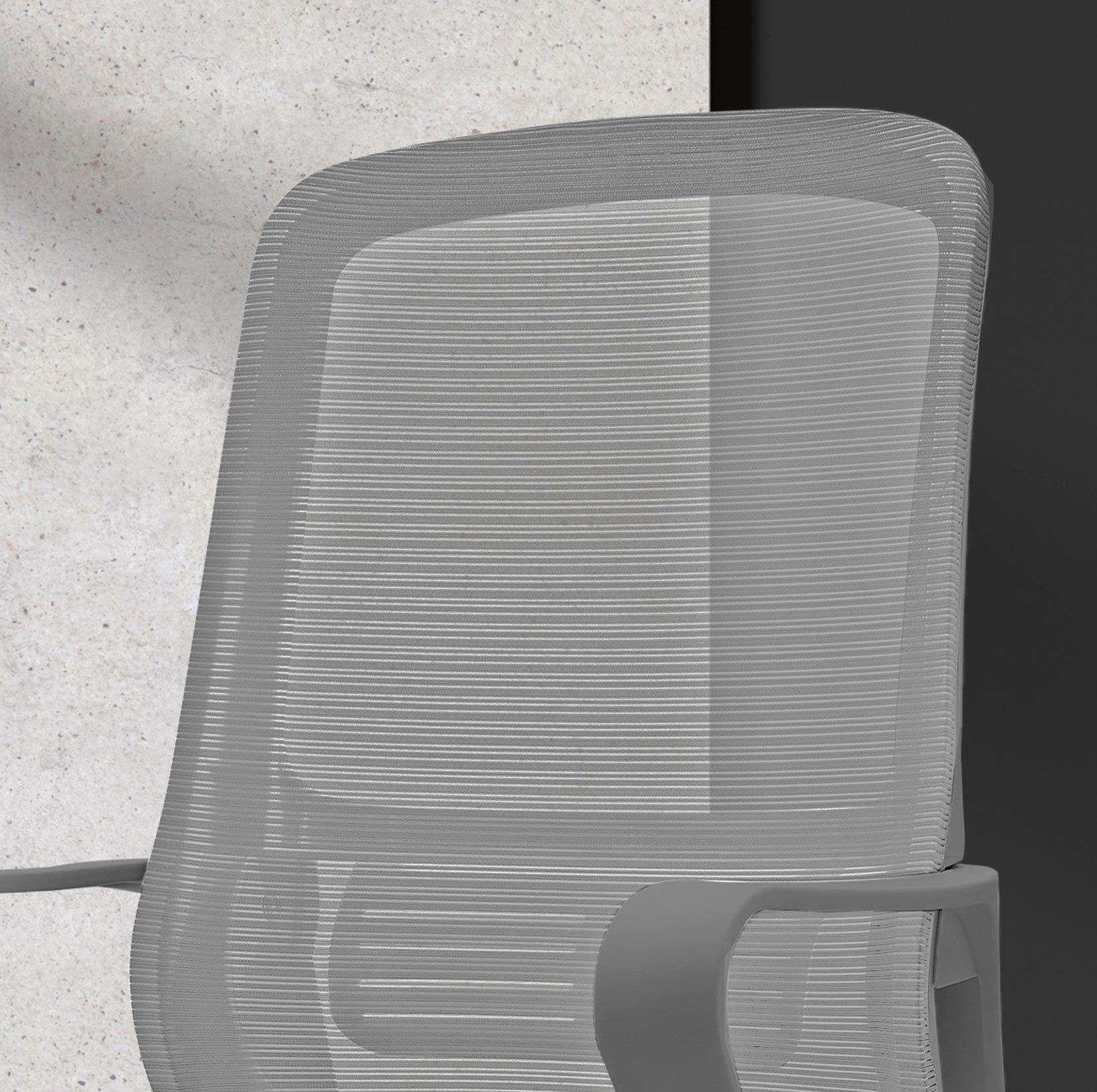 Respaldo de silla de malla gris con reposabrazos contra pared de hormigón.