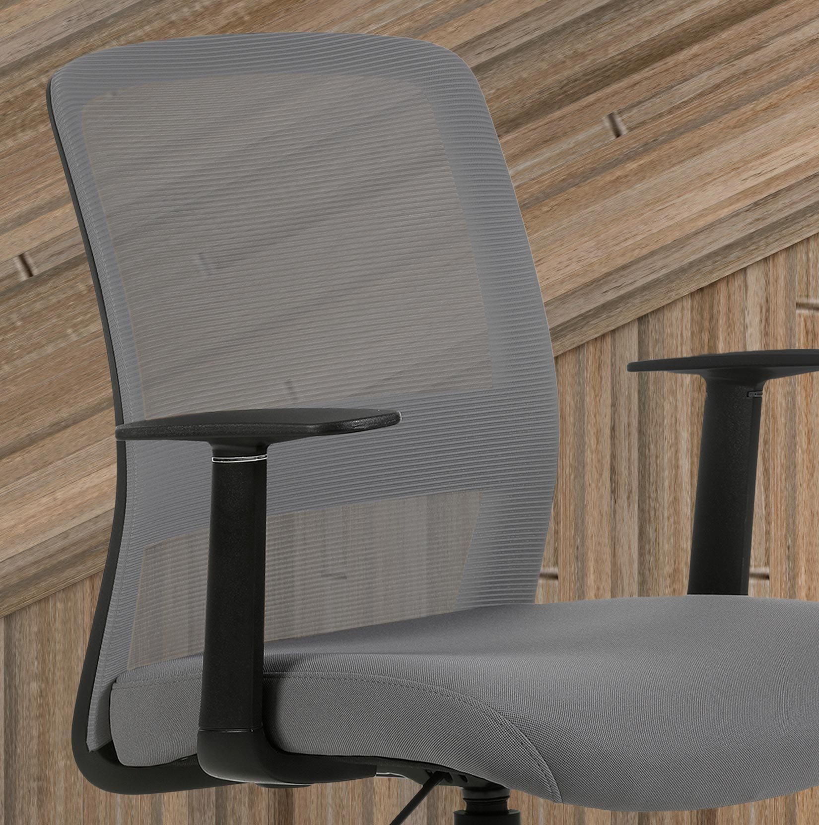 Silla de oficina gris con respaldo de malla, reposabrazos y asiento negros contra paneles de madera.
