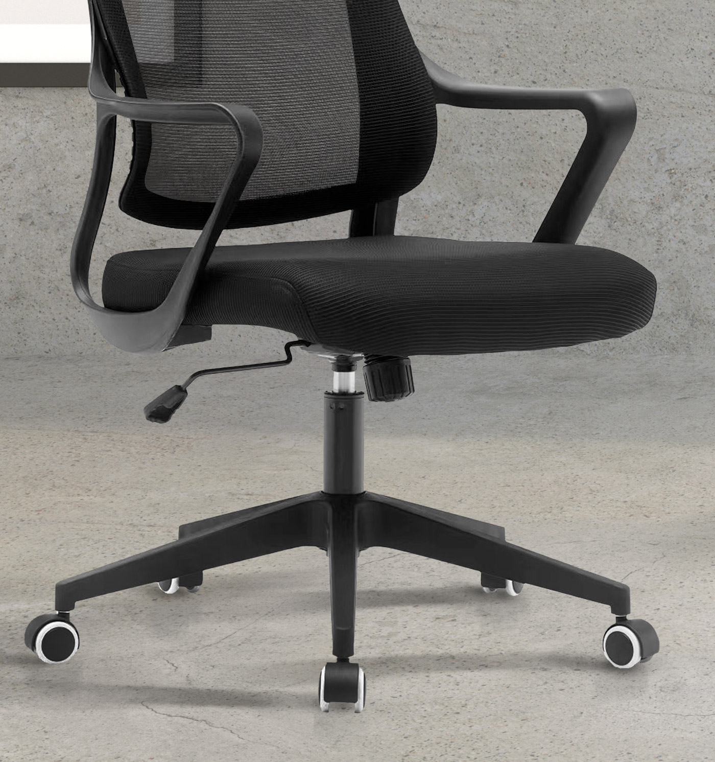 Una silla de oficina negra con respaldo de malla y asiento acolchado descansa sobre suelo de hormigón.