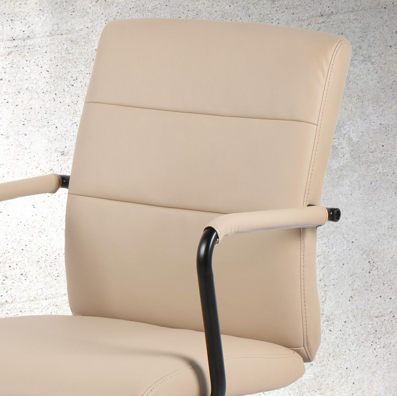 Silla de oficina beige con reposabrazos negros sobre pared de hormigón.
