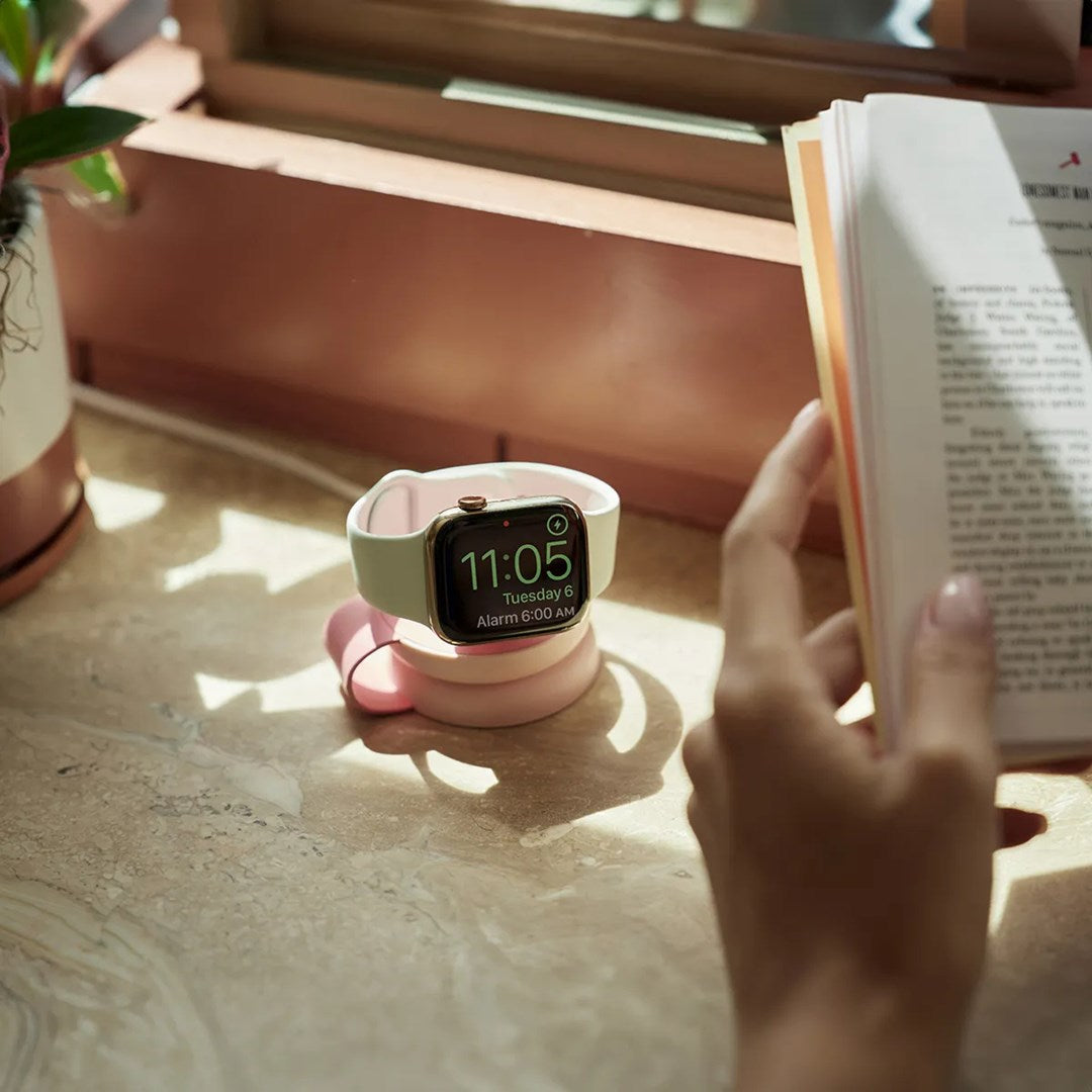Un orologio su un supporto di ricarica, con una persona che legge un libro nelle vicinanze.