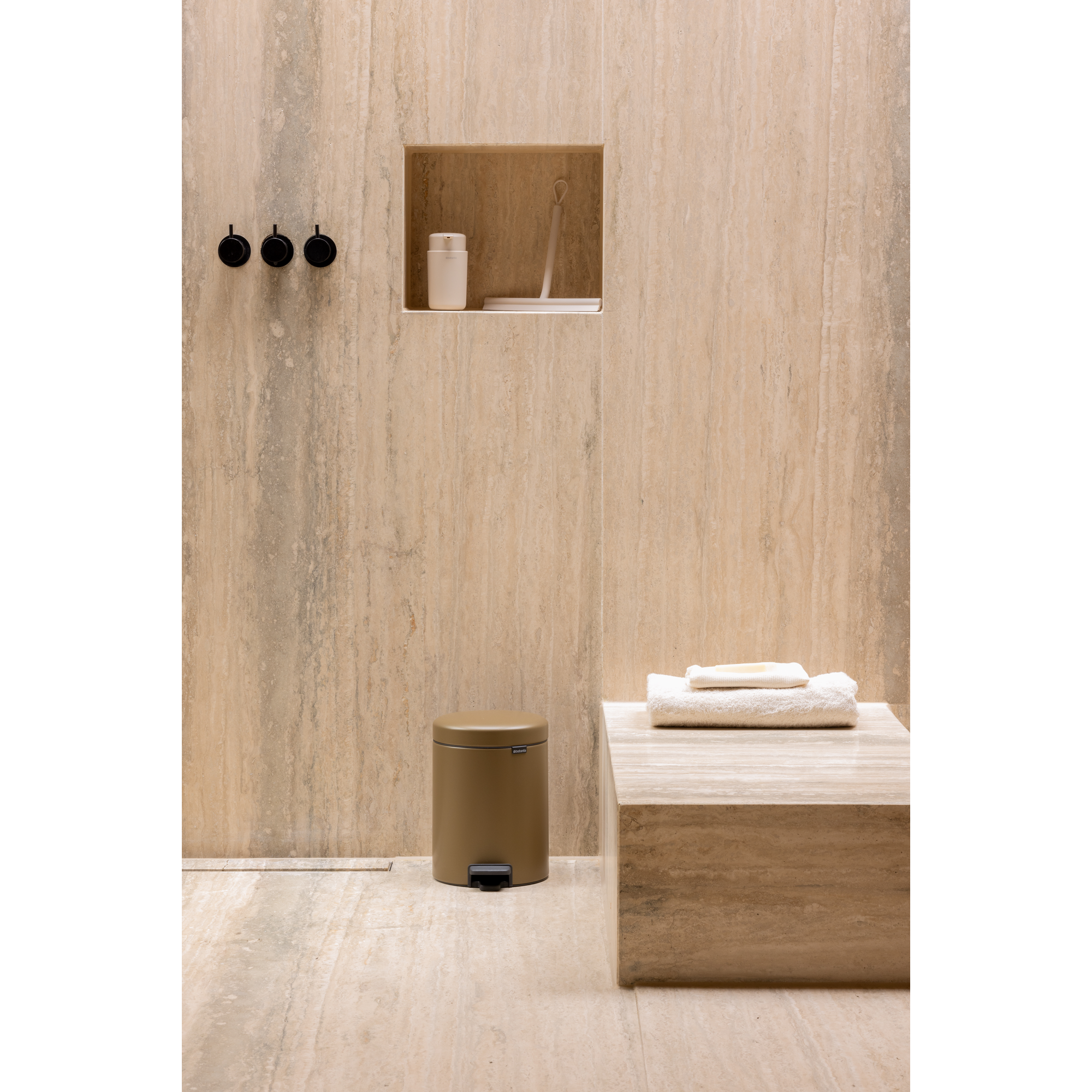 Badkamer met beige marmer, prullenbak, handdoeken en doucheaccessoires.