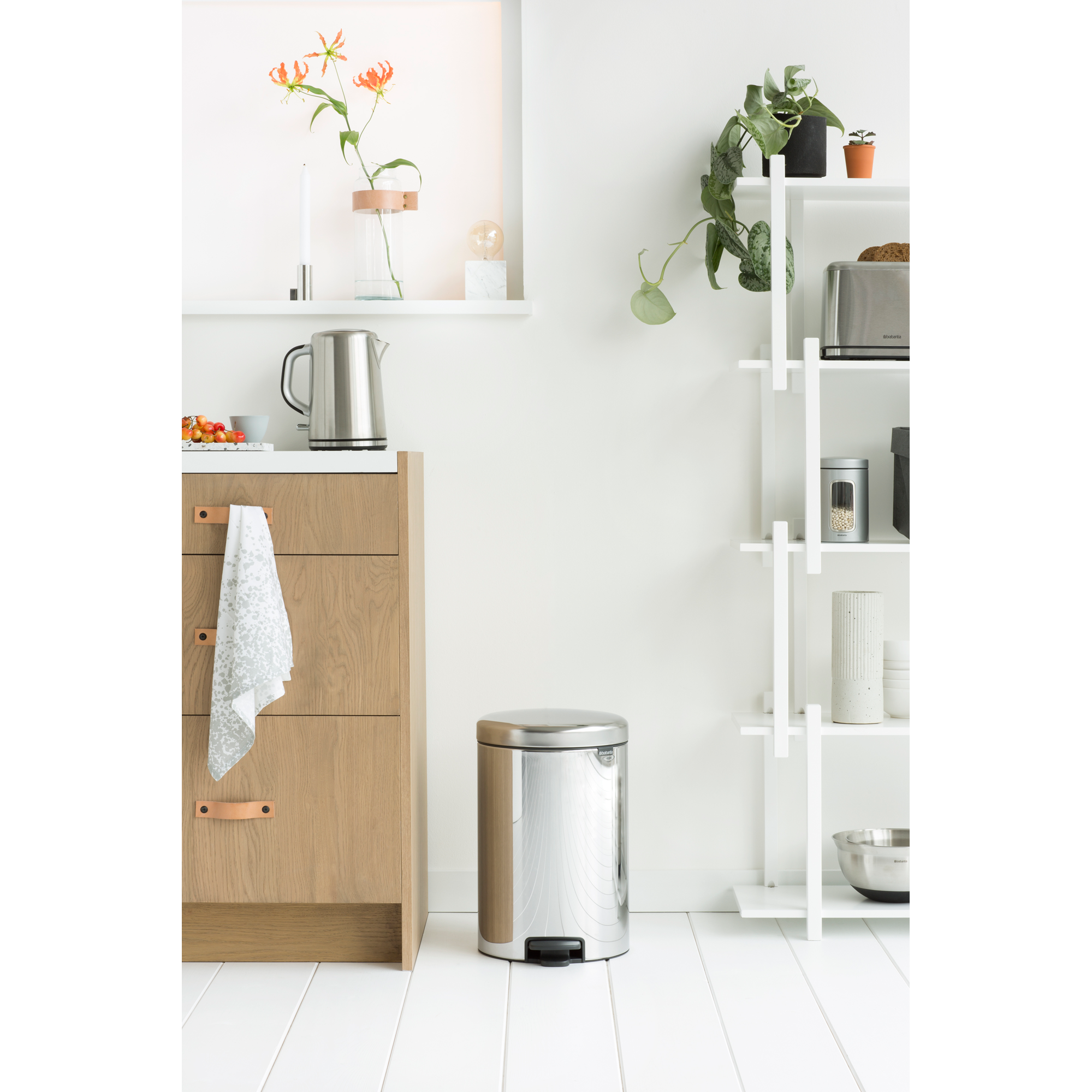 Een moderne keuken met houten lades, een zilveren prullenbak en een witte plankeneenheid.