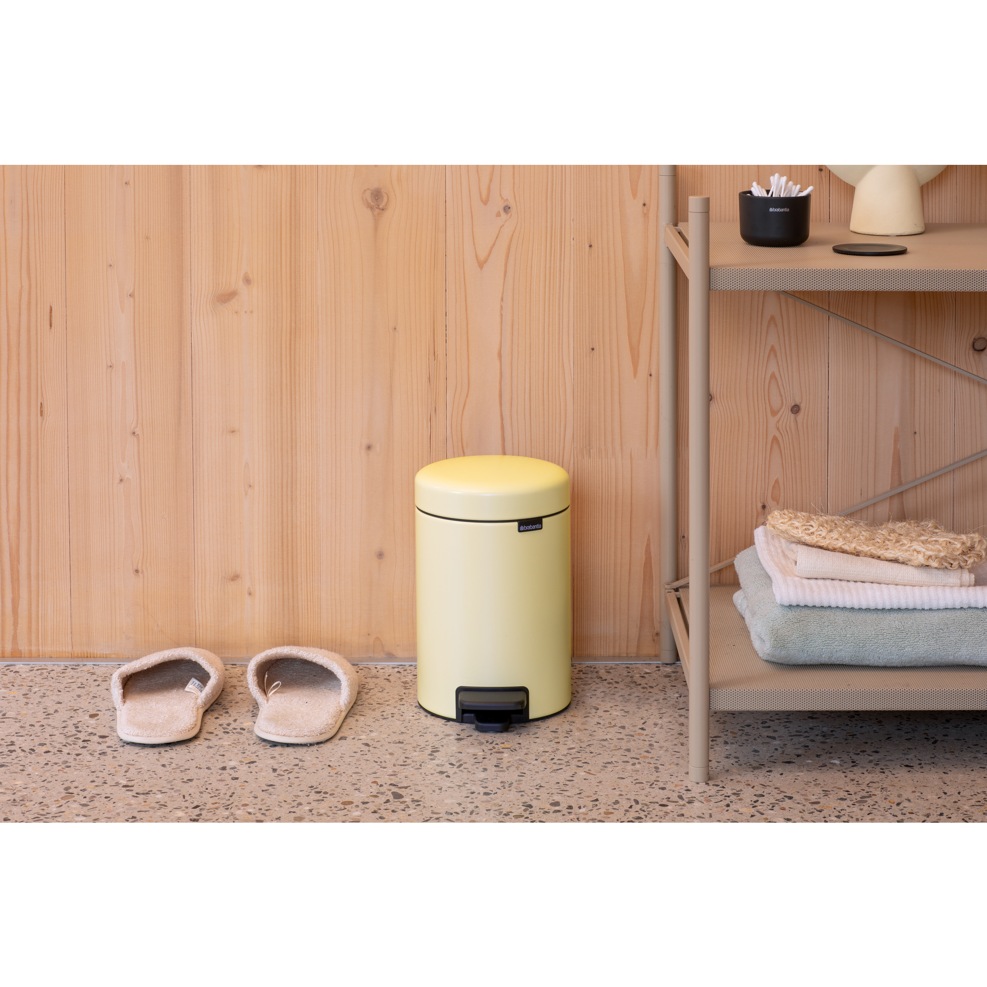 Un cubo amarillo pálido está con zapatillas frente a una pared de madera.