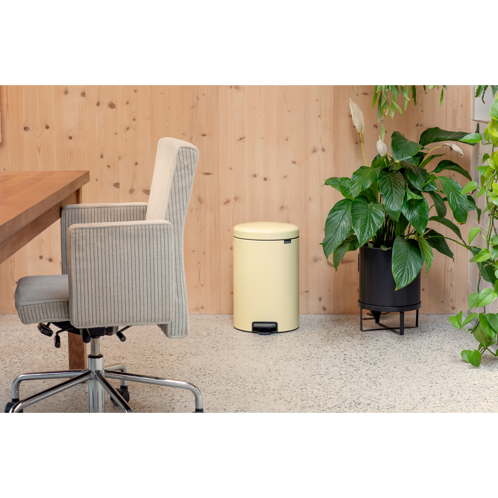 Silla de oficina color crema junto a escritorio de madera, papelera amarilla y planta.