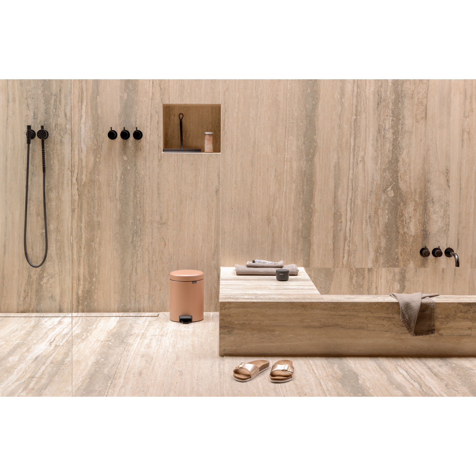 Een stijlvolle badkamer met beige tegels, douche, prullenbak en sandalen.