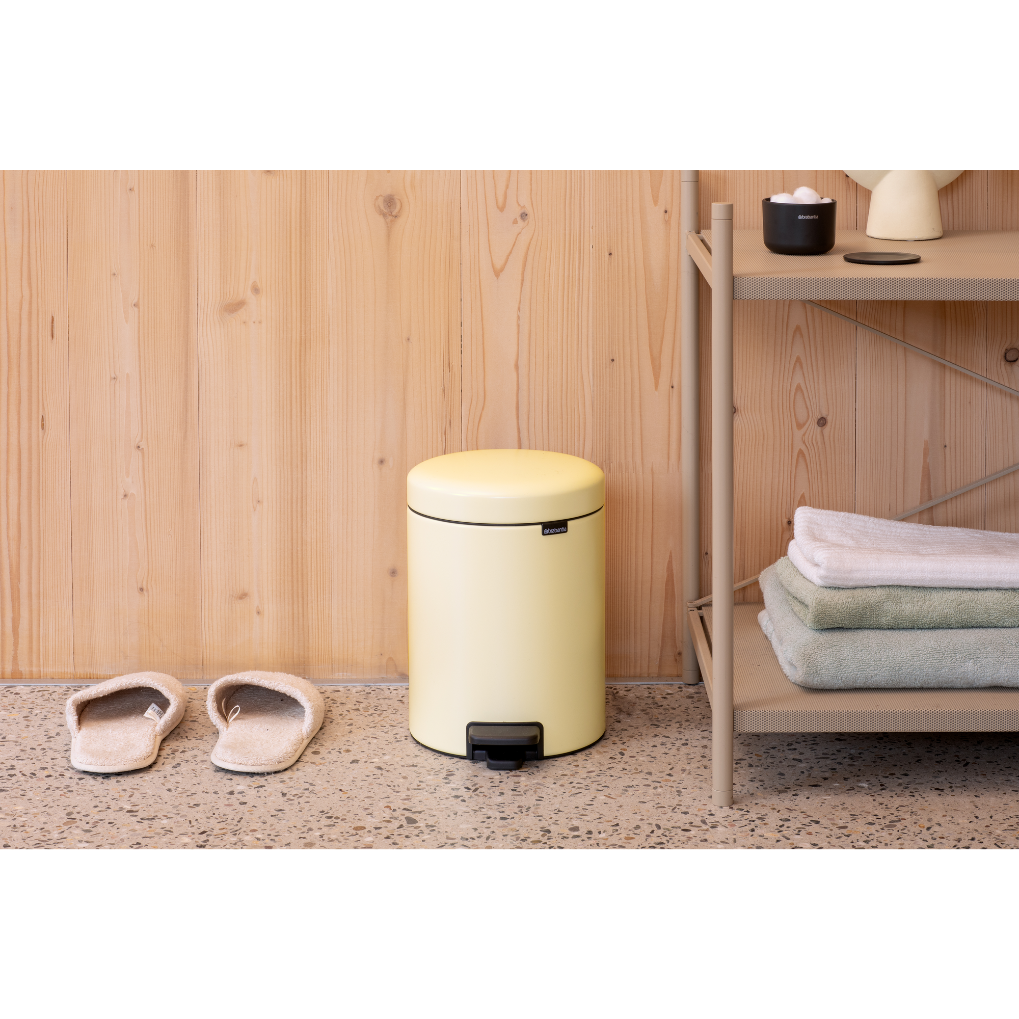Un cubo de pedal amarillo junto a dos zapatillas frente a una pared de madera.