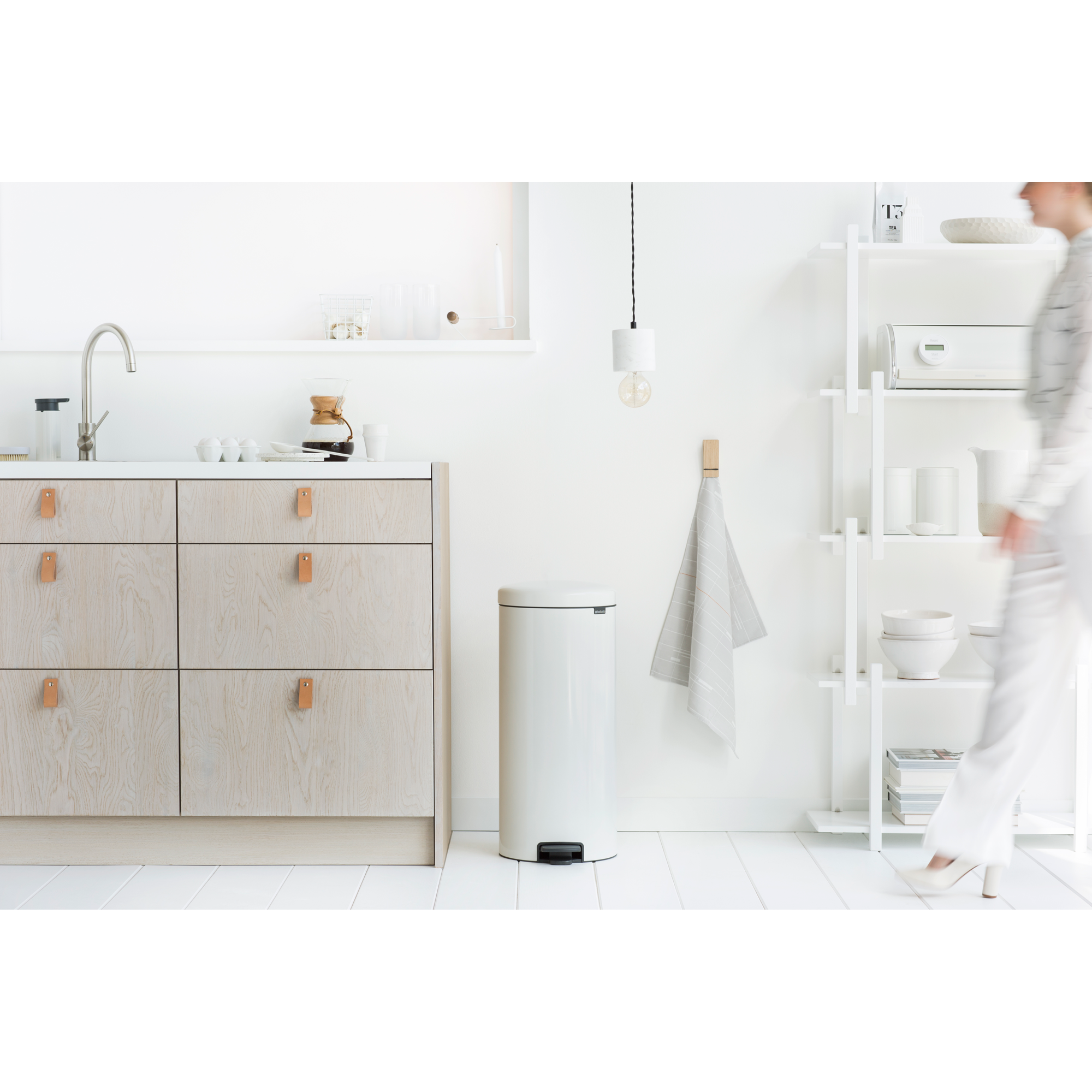 Lichte keuken met houten kasten, prullenbak, plank en een persoon.