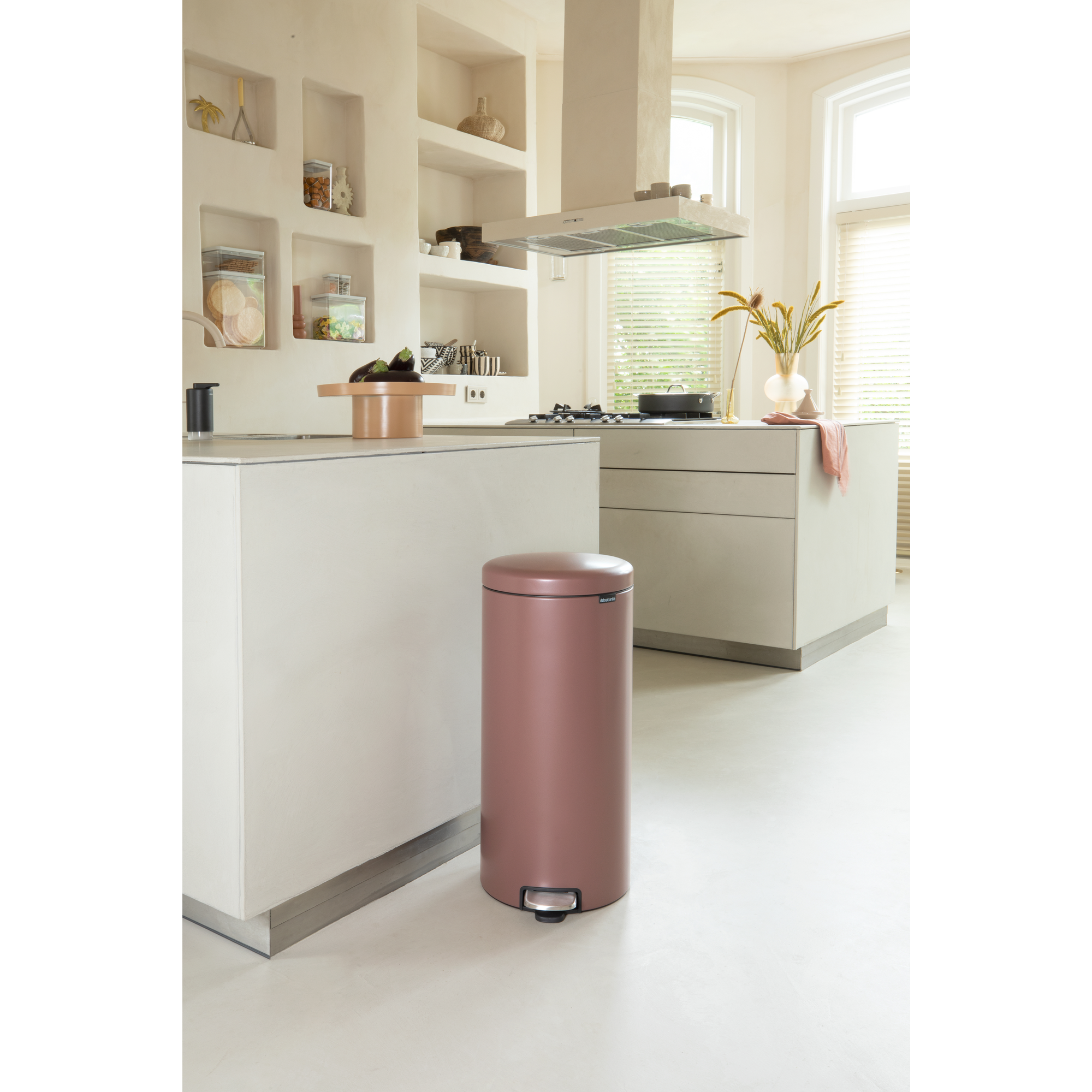 Een roségouden prullenbak met een voetpedaal staat in een moderne keuken naast een aanrecht.
