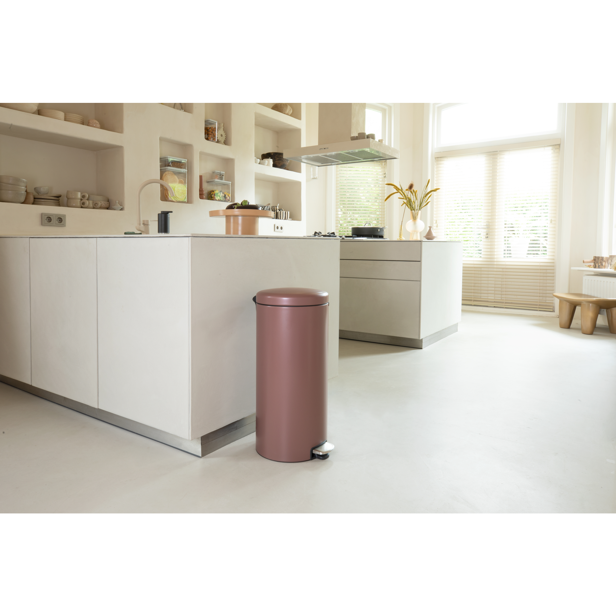 Een roze prullenbak staat in een moderne keuken met witte kasten.