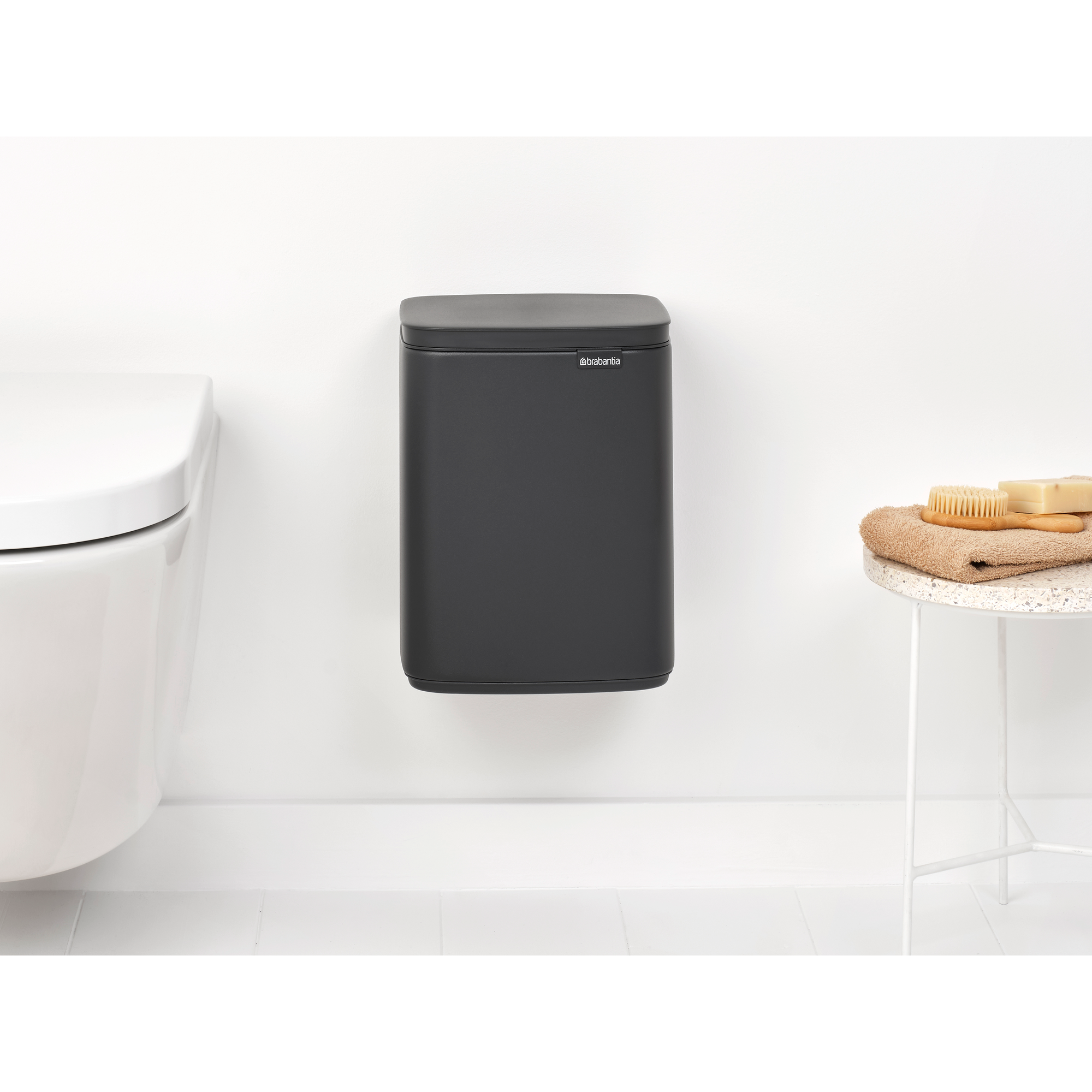 Een donkere wandprullenbak naast een wit toilet en een bijzettafel.
