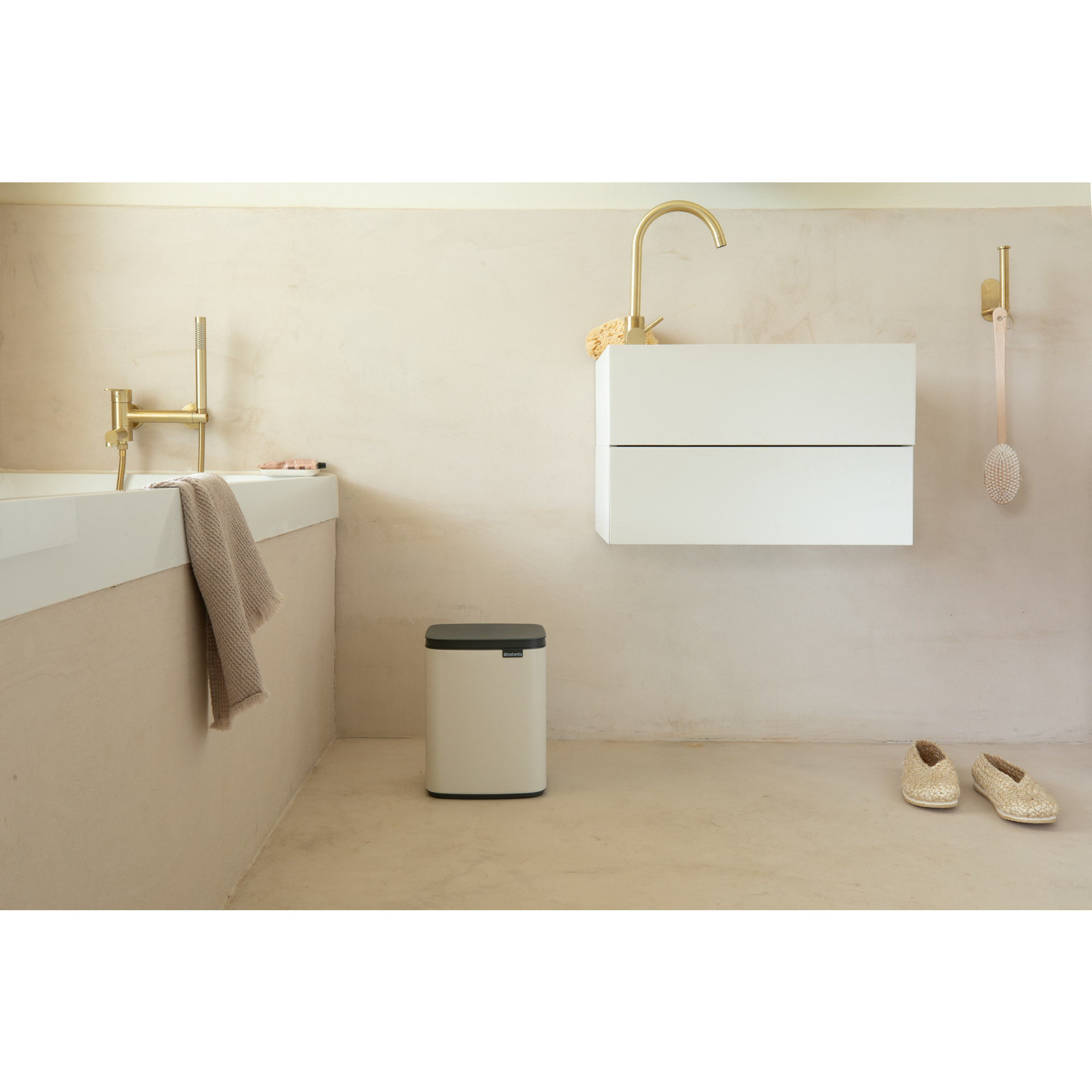 Moderne badkamer met ligbad, wastafel, prullenbak en gouden kranen.