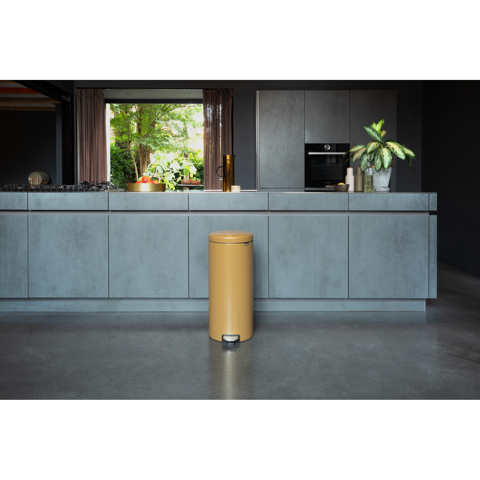 Een gele pedaalemmer in een moderne keuken met grijze kasten en uitzicht op een raam.