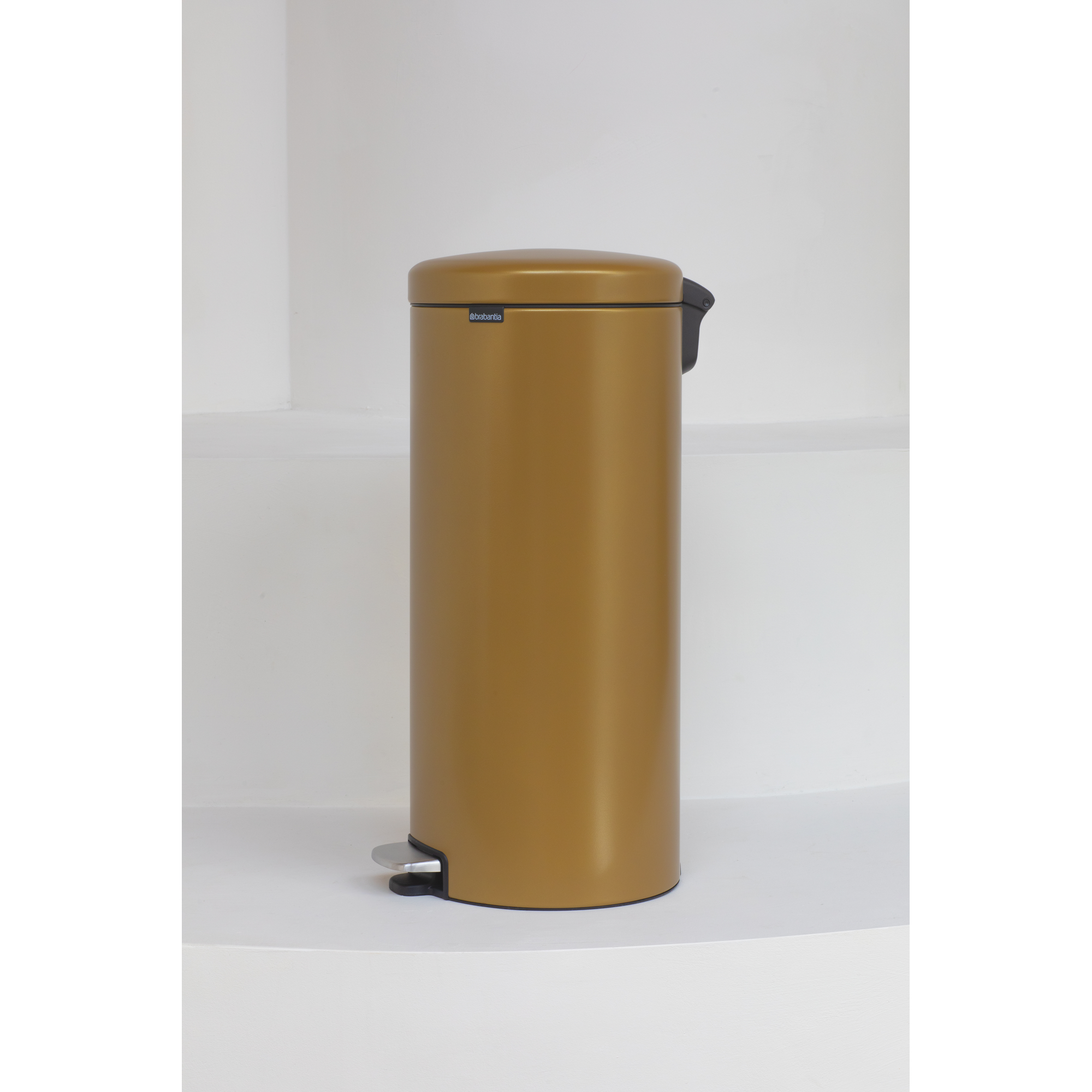Een gouden prullenbak met een zilveren pedaal staat op een witte ondergrond.