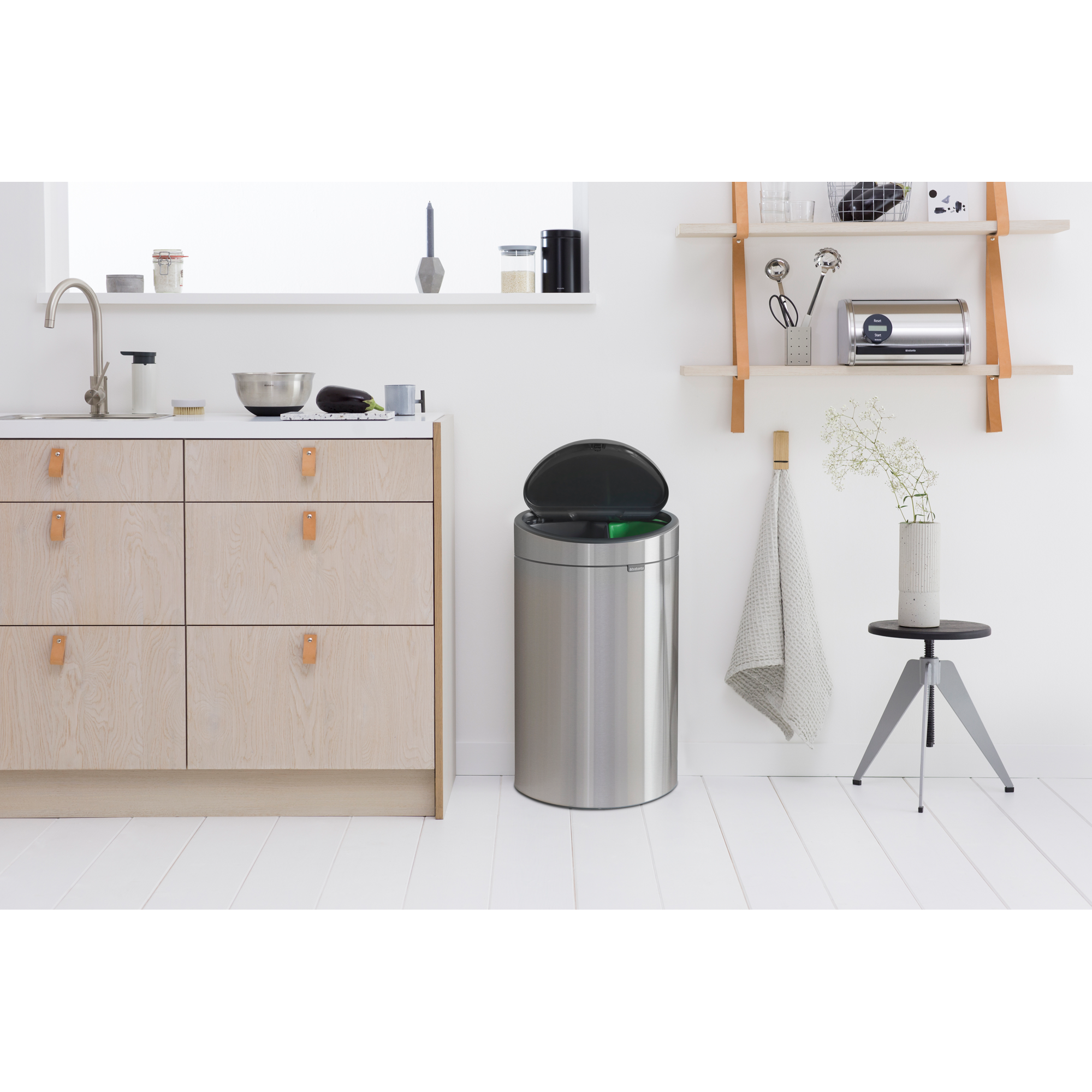 Een open zilveren prullenbak met groene inhoud staat naast houten keukenkastjes.