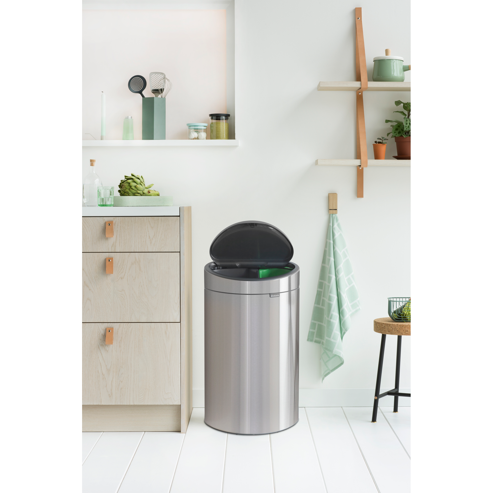 Een glimmende prullenbak naast houten kasten in een lichte keuken.