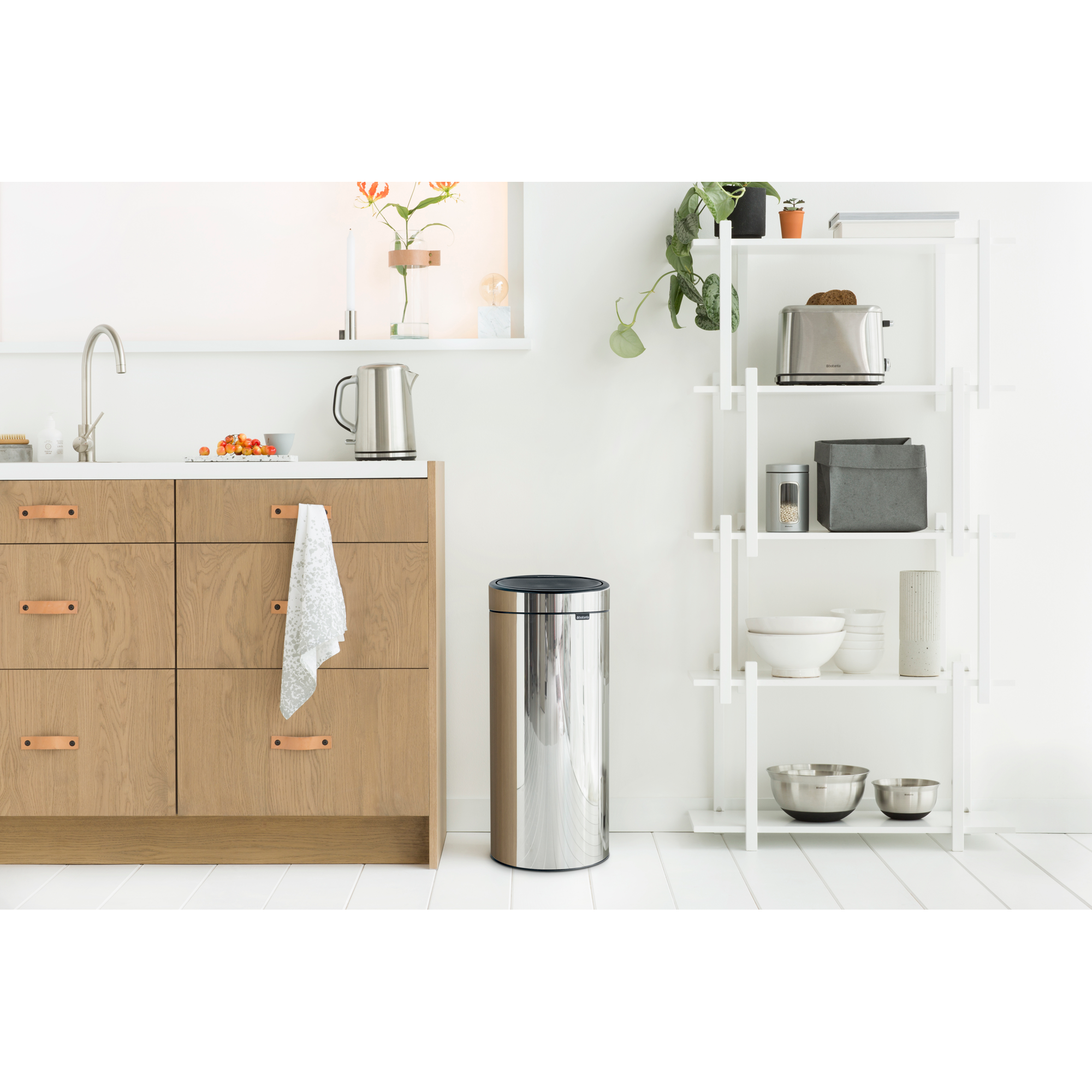 Een moderne keuken met houten kasten, een zilveren prullenbak en een plank met keukengerei.