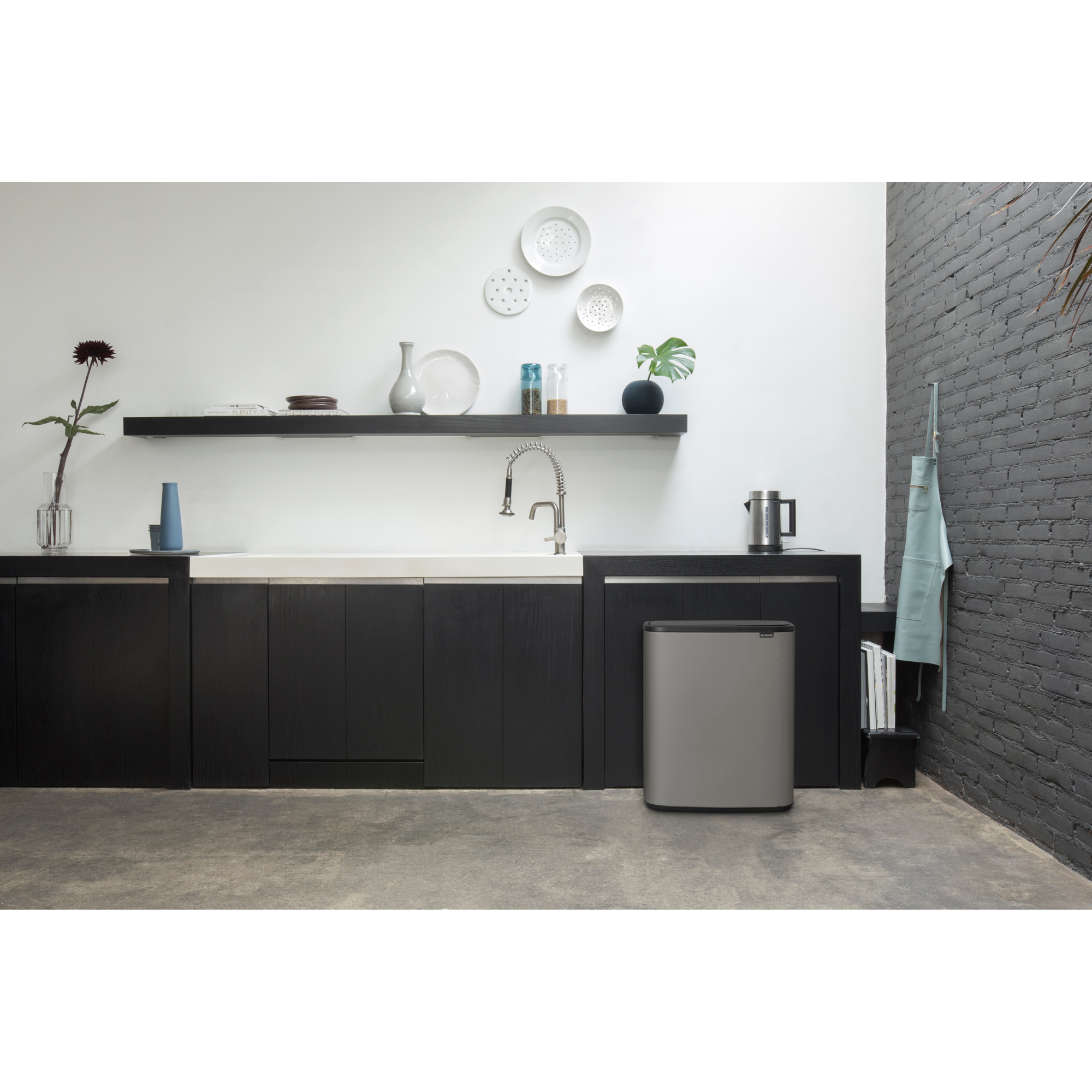 Moderne keuken met donkere kasten, gootsteen, zilveren prullenbak en bakstenen muur.