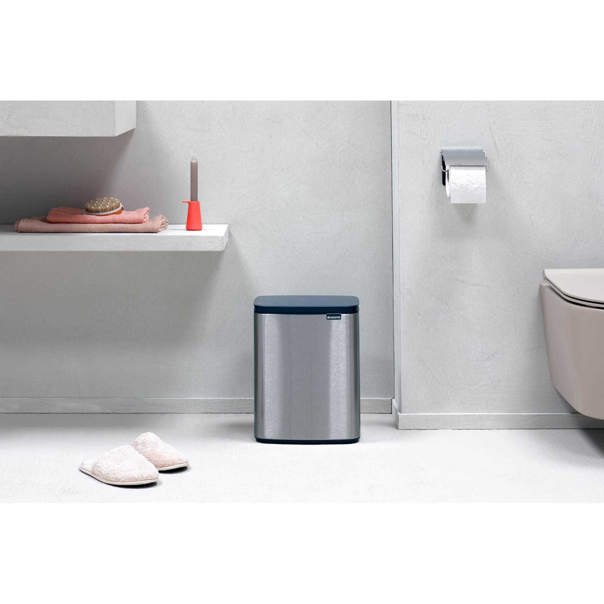 Een zilveren prullenbak met blauw deksel naast een toilet. Pantoffels ervoor.