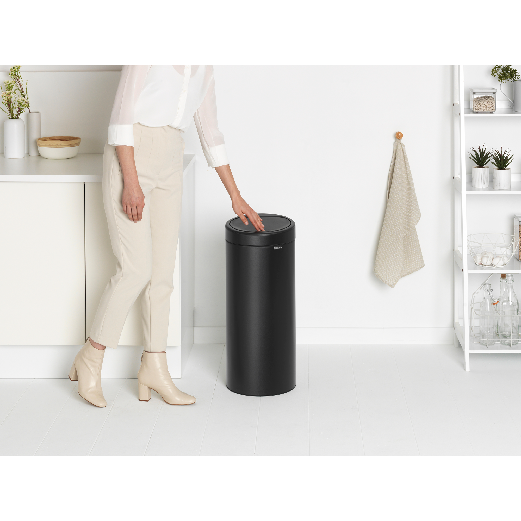 Een vrouw raakt een zwarte sensor prullenbak aan in een lichte kamer.