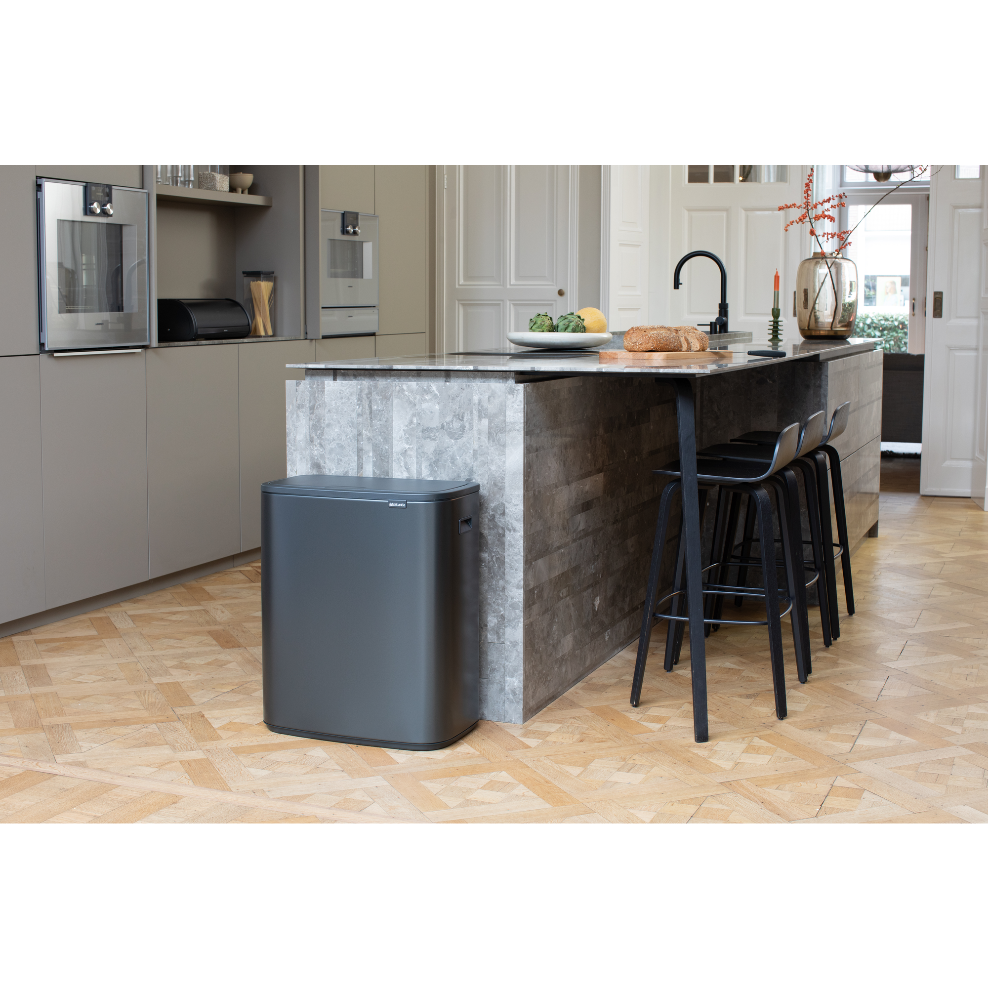 Een moderne grijze keuken met roestvrijstalen apparaten en een marmeren eiland met barkrukken.