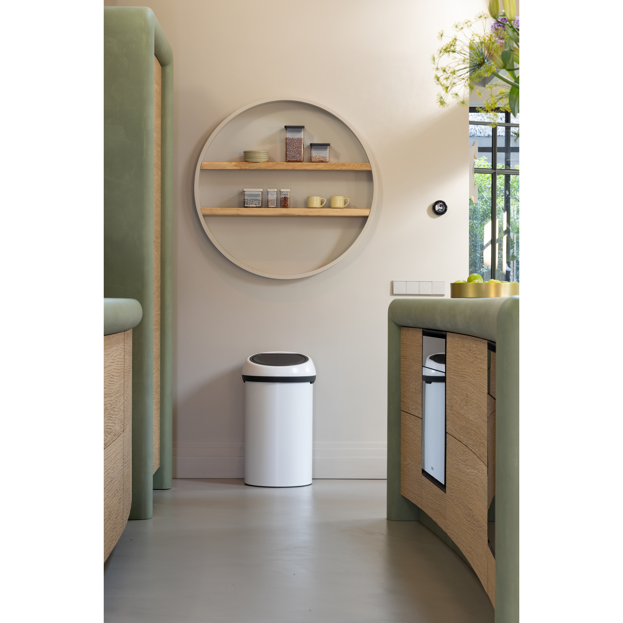 Moderne keuken met groene kasten, een witte prullenbak en ronde planken.