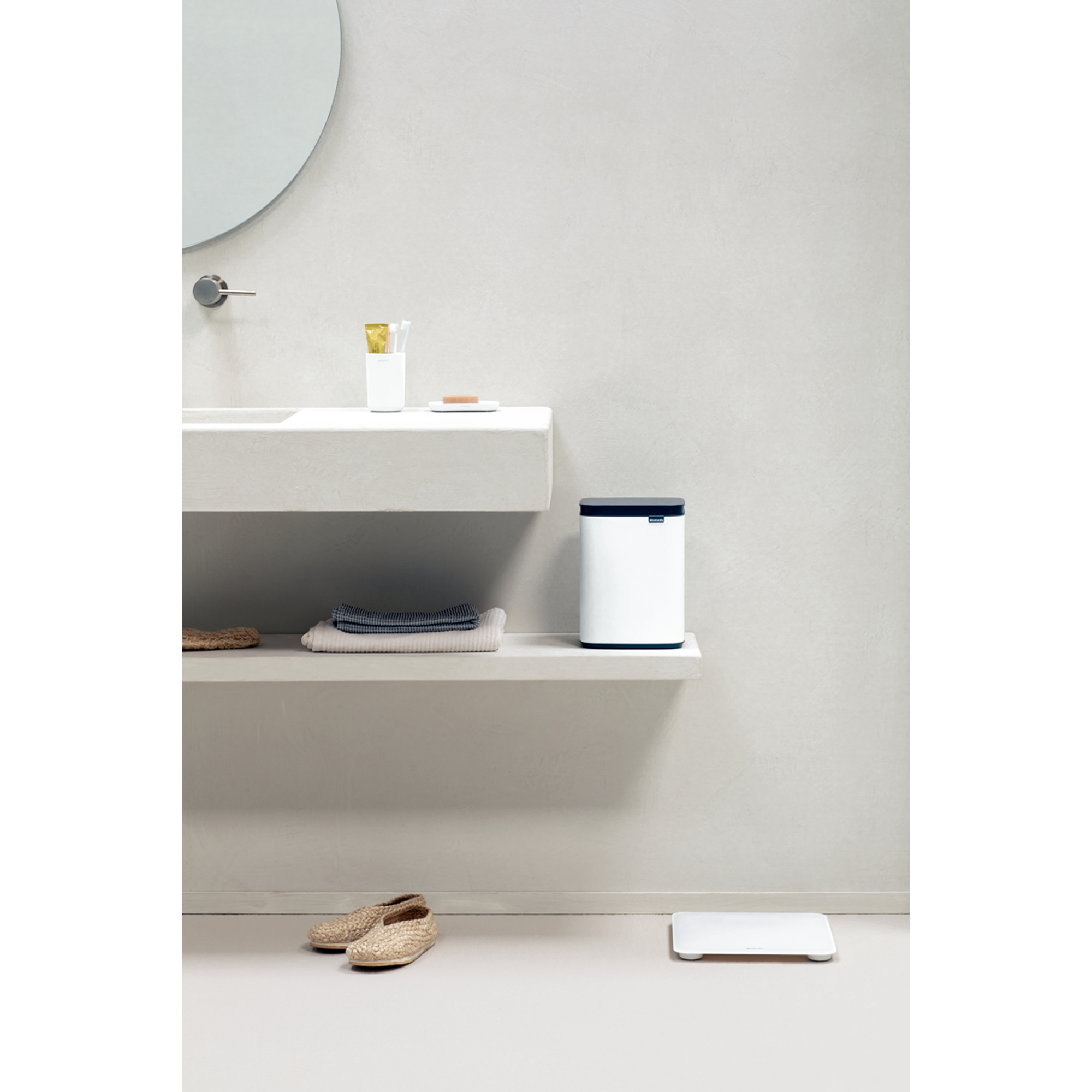Minimalistische badkamer met witte prullenbak, handdoeken, weegschaal en schoenen.