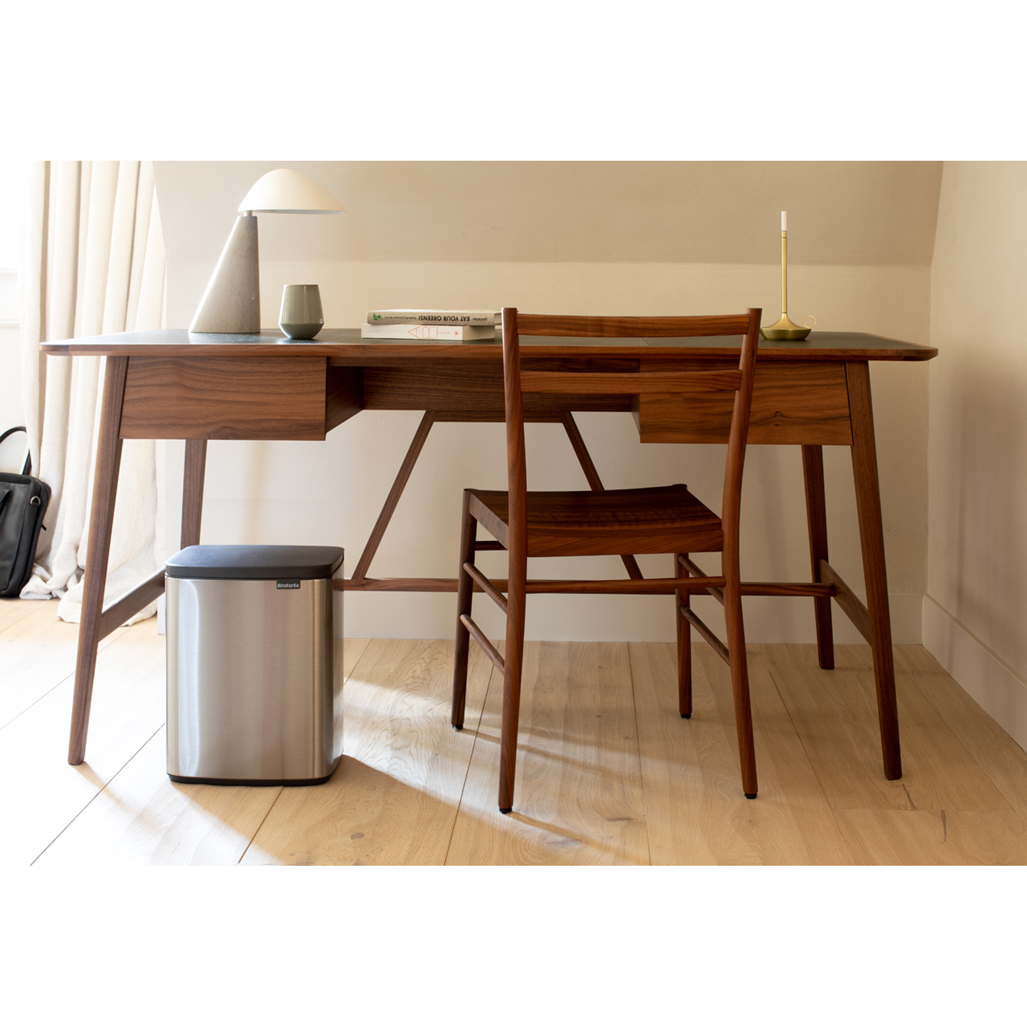 Een houten bureau met lamp, vaas, boeken, stoel en prullenbak.