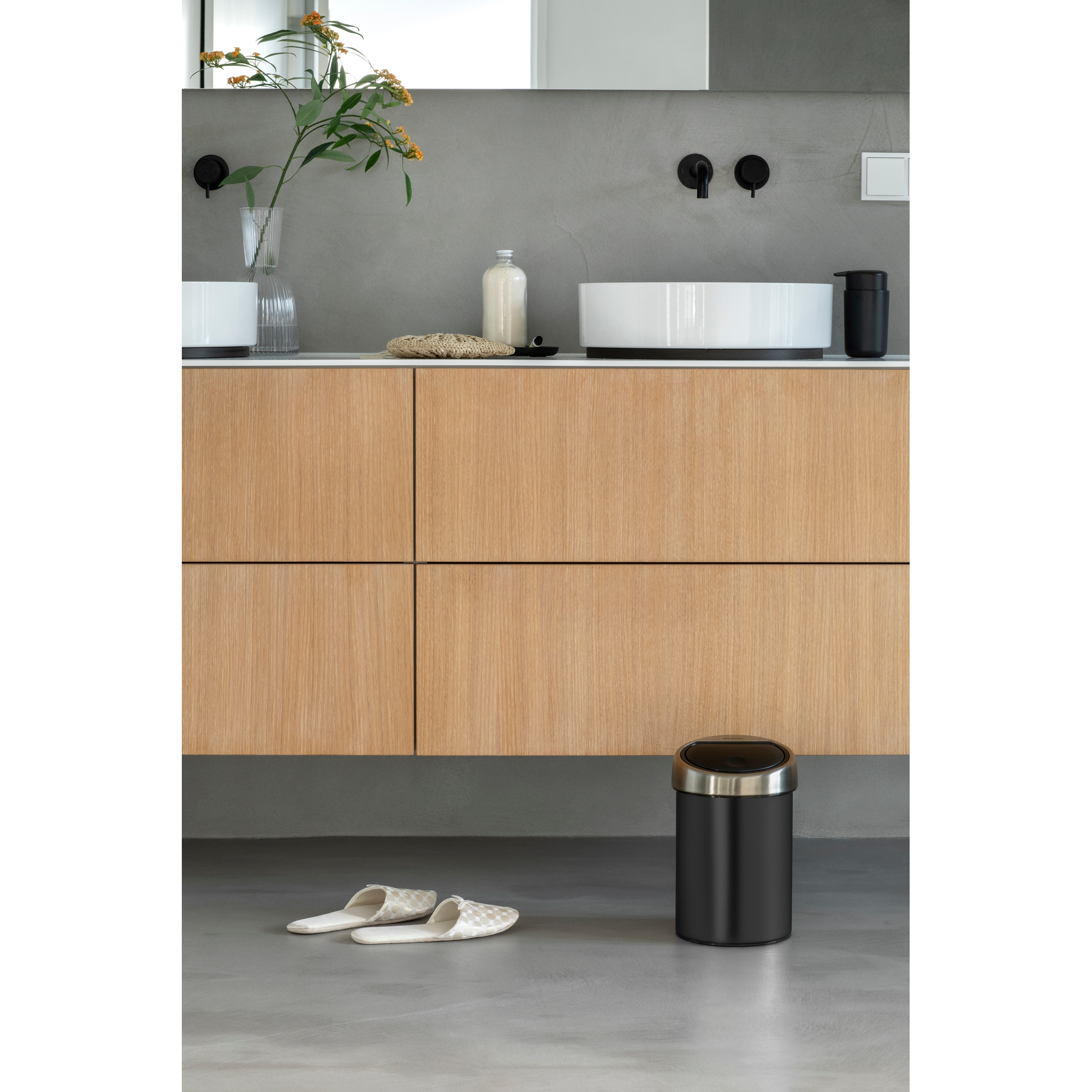 Een badkamer met houten wastafelmeubel, wasbak, zeepdispenser, prullenbak en pantoffels.