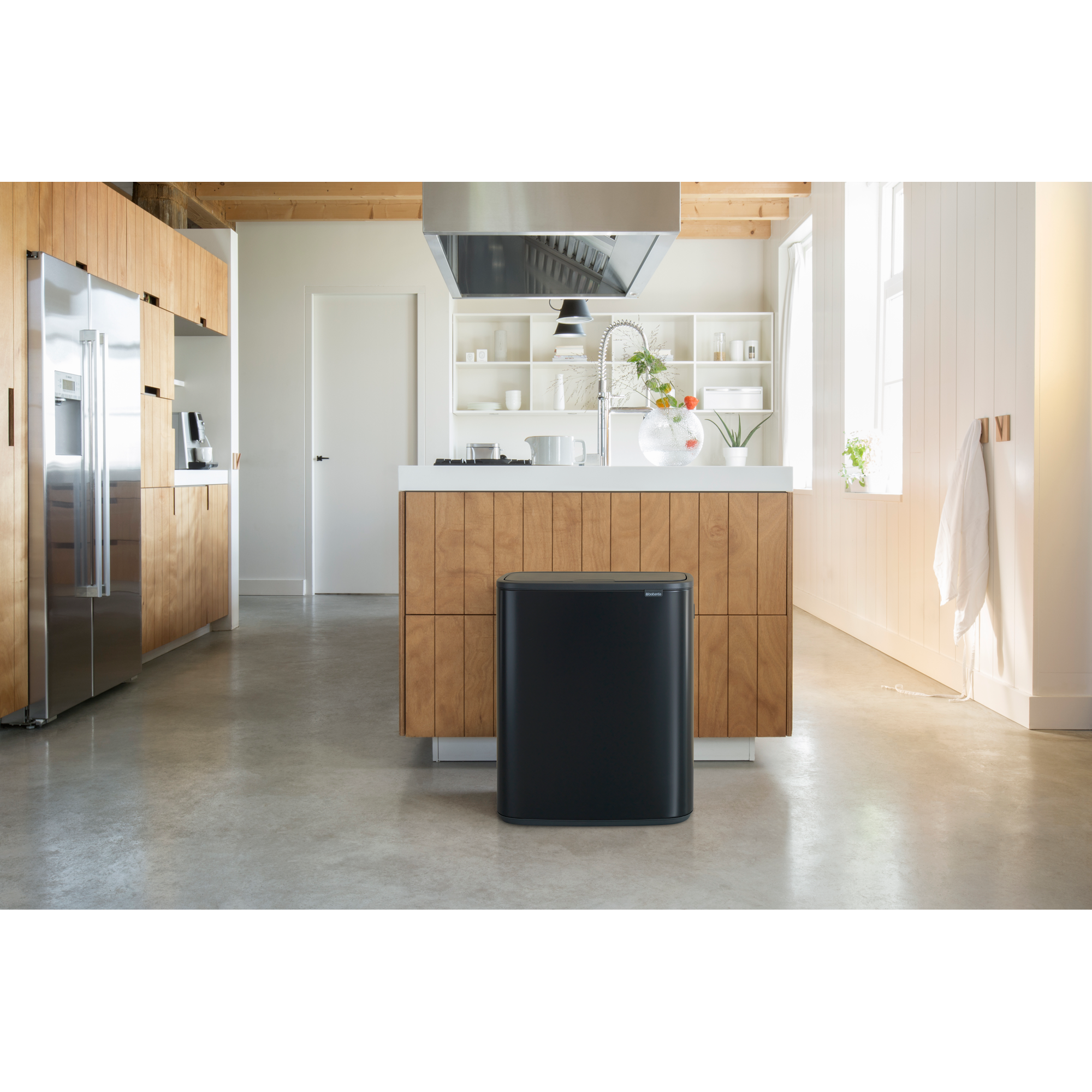 Een zwarte prullenbak voor een houten keuken met roestvrijstalen koelkast.