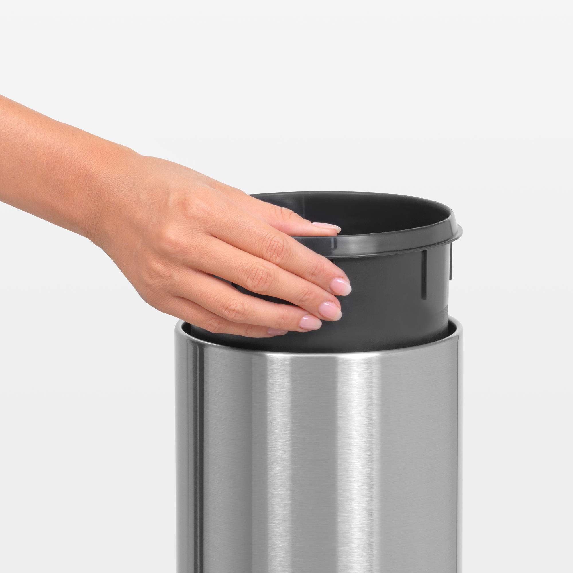 Een hand plaatst een zwarte inzet in een zilveren prullenbak.