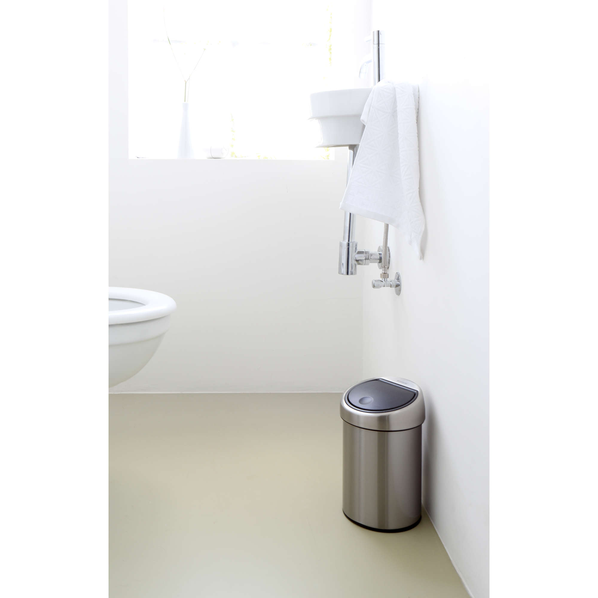 Een zilveren prullenbak met zwart deksel staat naast een toilet en wastafel.