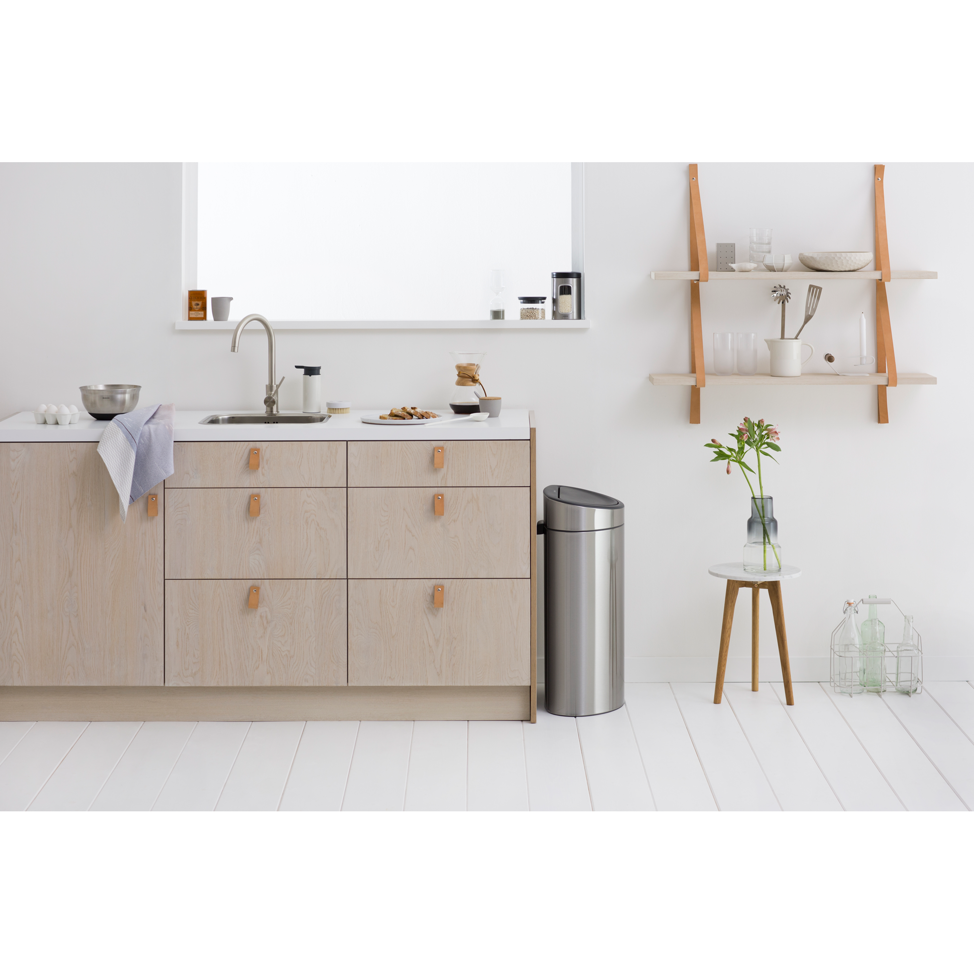 Een lichte keuken met houten kasten, gootsteen, lades en een prullenbak.